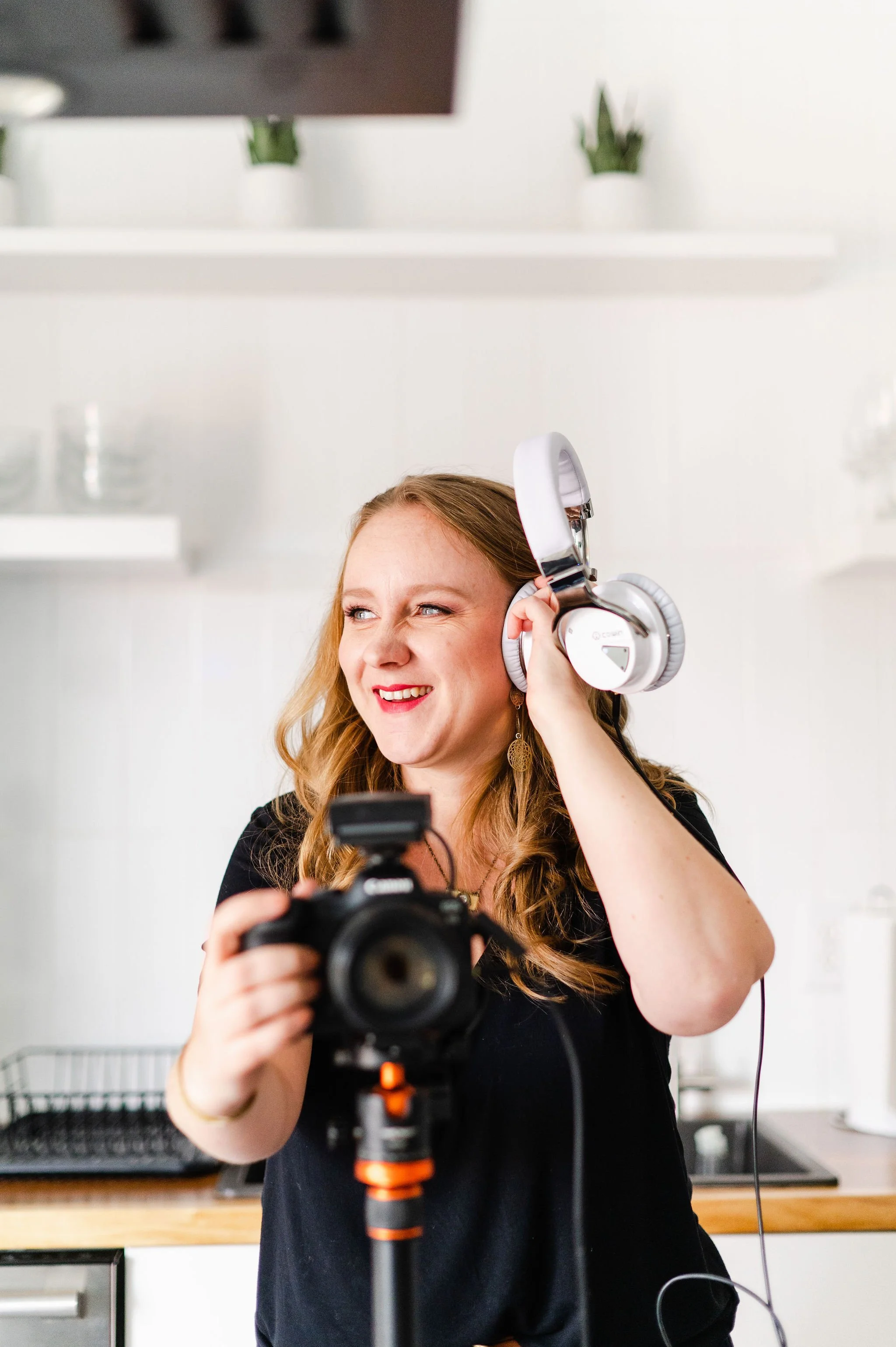 Brand photographer in a black shirt holds a camera in one hand and headphones up to her ear in another hand in this Los Angeles branding photo.