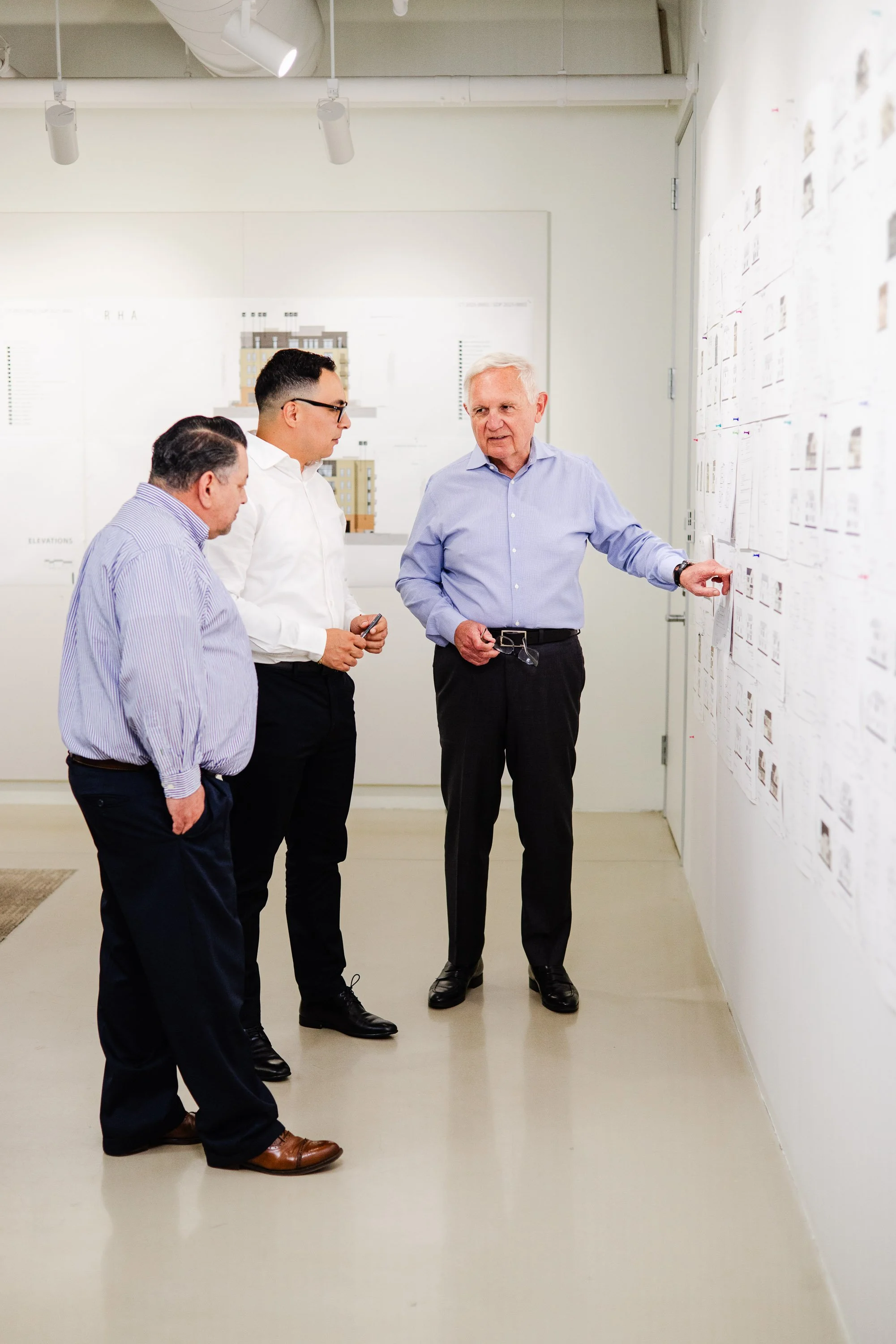 Three Robert Hidey Architects colleagues discuss architectural drawings displayed on the office wall.