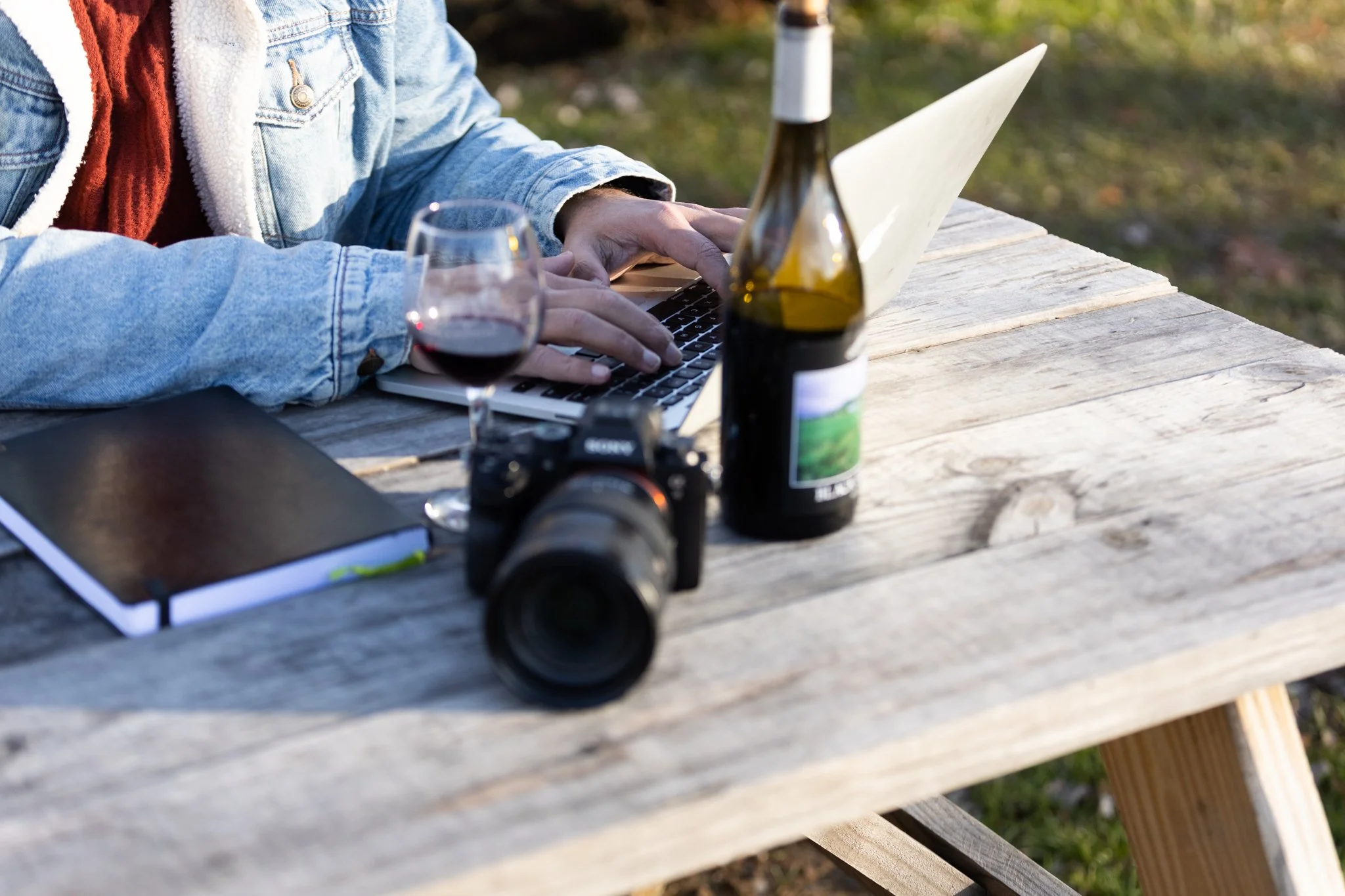 A man sits at a table with a bottle of wine, laptop, and camera, for this NJ brand photo shoot.