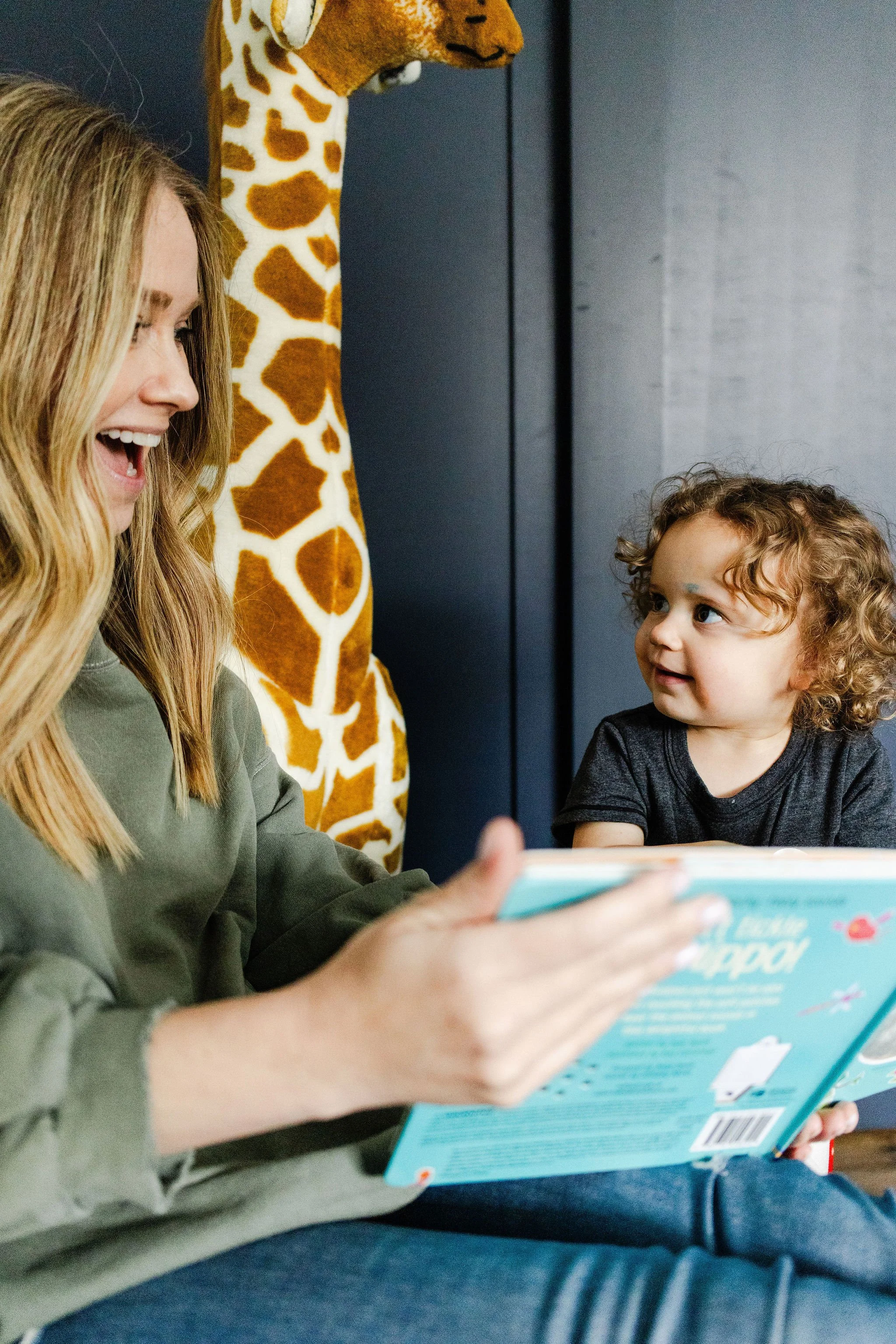Sleep pediatrician reads aloud with a toddler during a cozy in-home brand session, styled with playful props like a giant giraffe.