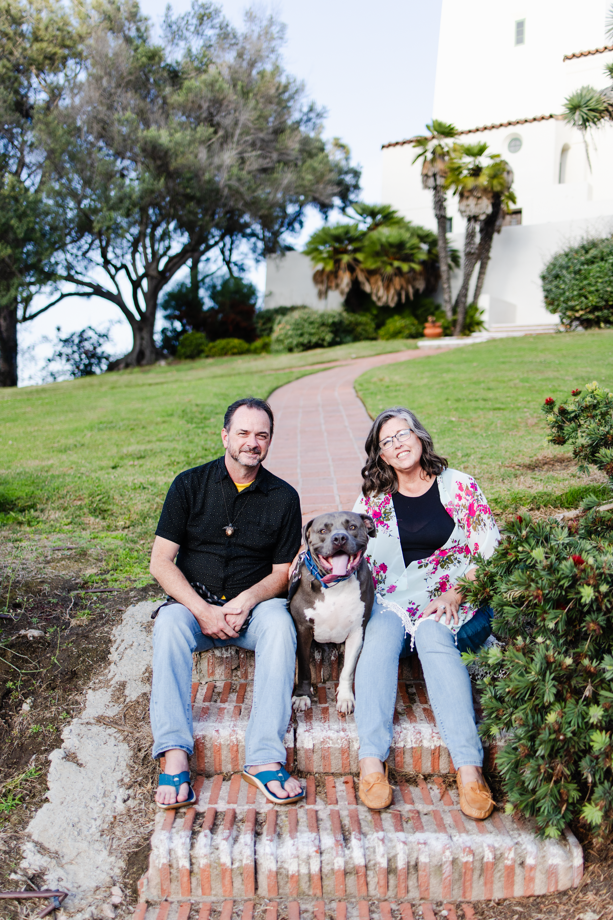 A family portrait of an LMFT, her partner, and her dog in front of a walkway for her therapy business's brand photo session.