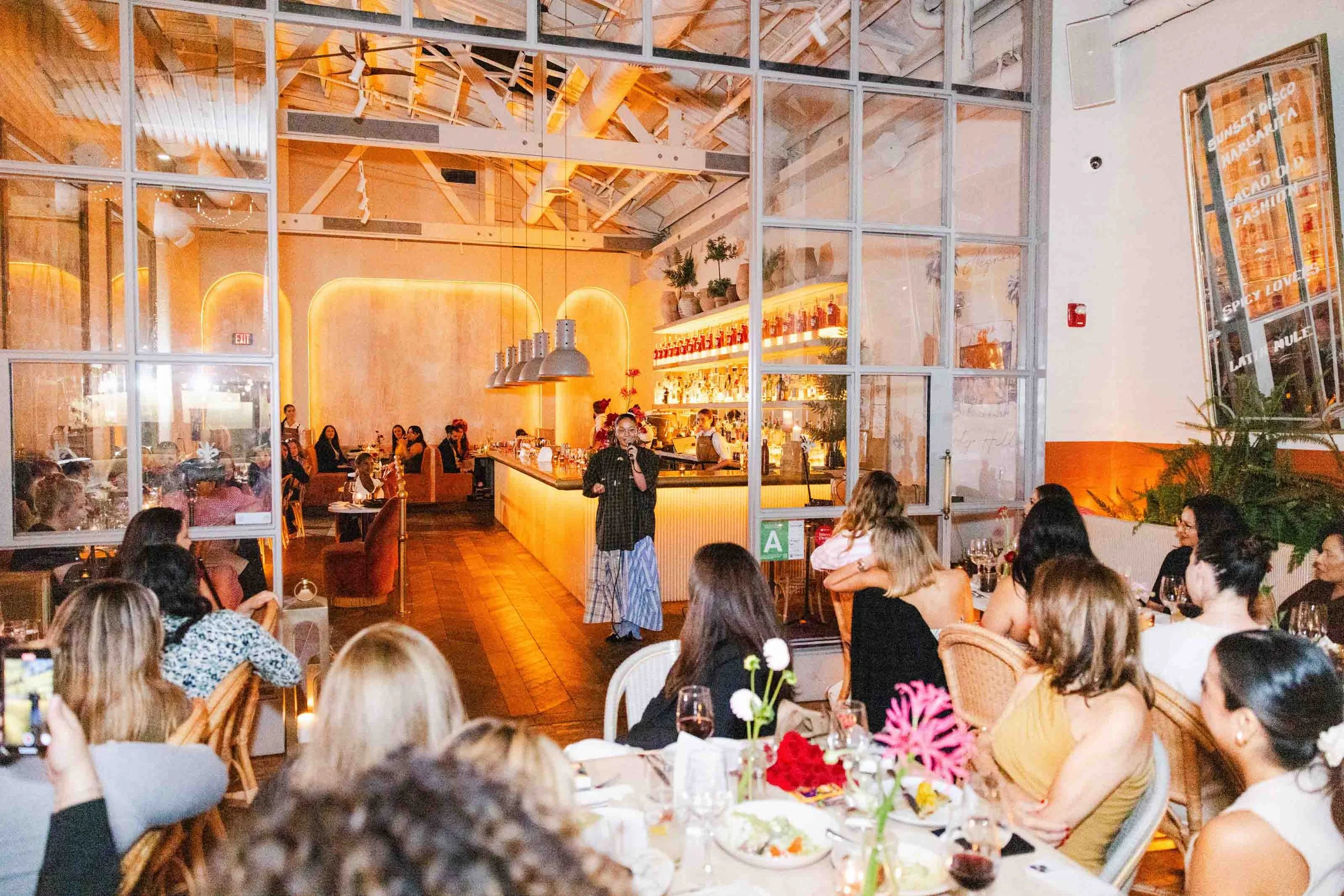 Wide-angle shot of the Latinas in Beauty launch event at Negroni Cafe, showing attendees listening to a speaker, captured for nonprofit event photography.