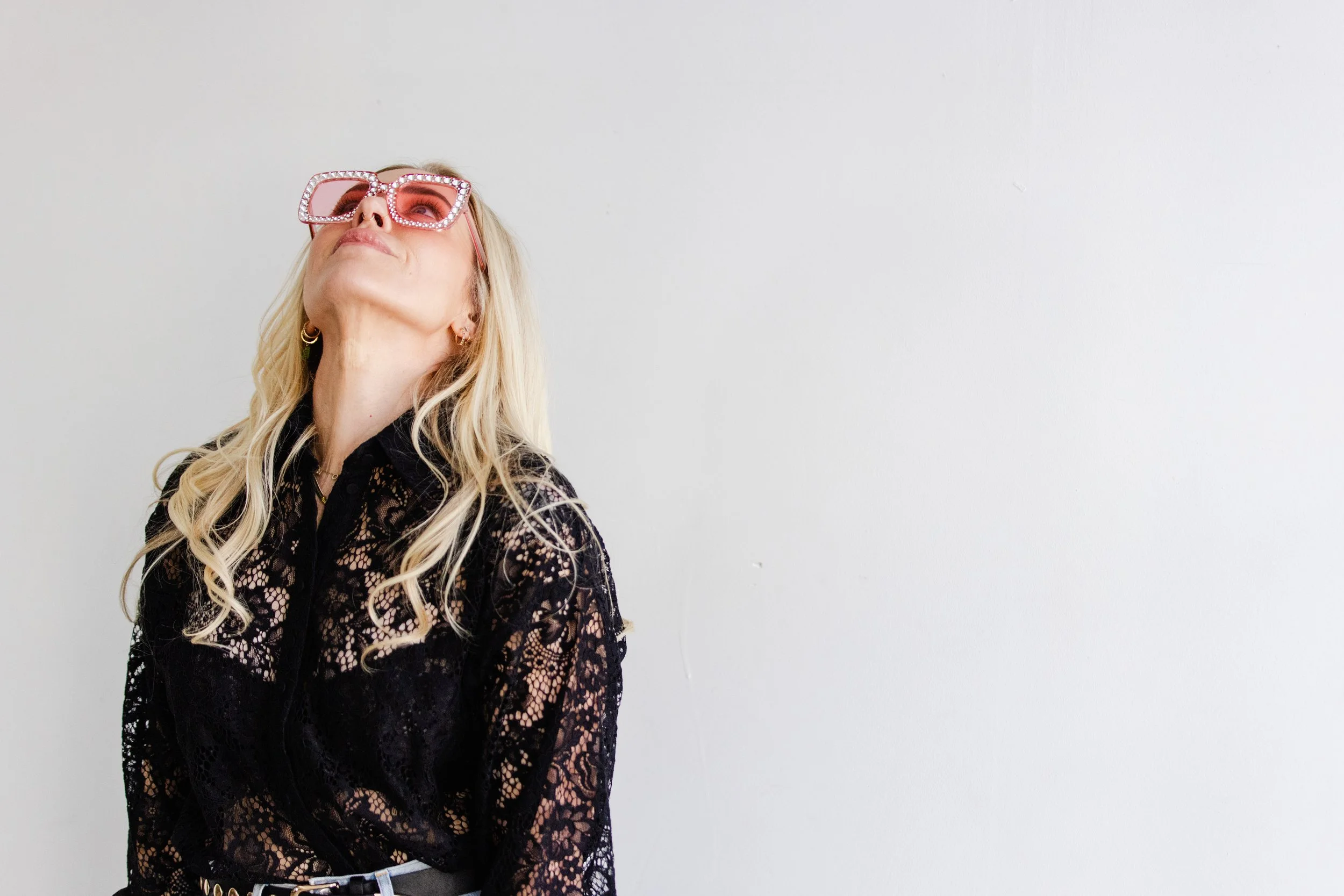 Confident woman business coach wearing bold pink sunglasses and a black lace blouse, looking up and smiling during a branding photo session in LA.