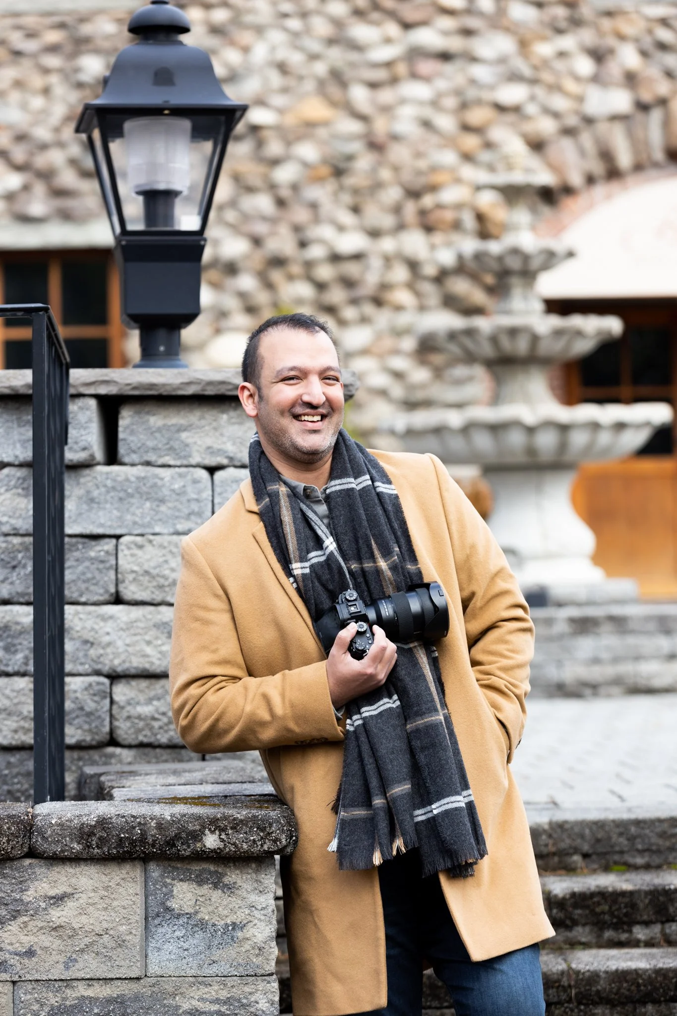 Branding photo of a man in a mustard jacket and black jeans posing confidently in front of a stone wall during a NJ brand photoshoot