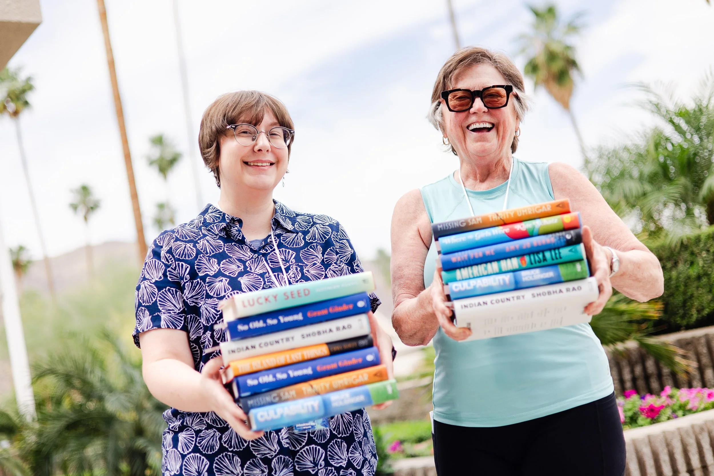 Two attendees holding stacks of books outdoors at the Palm Springs Book Fest.
