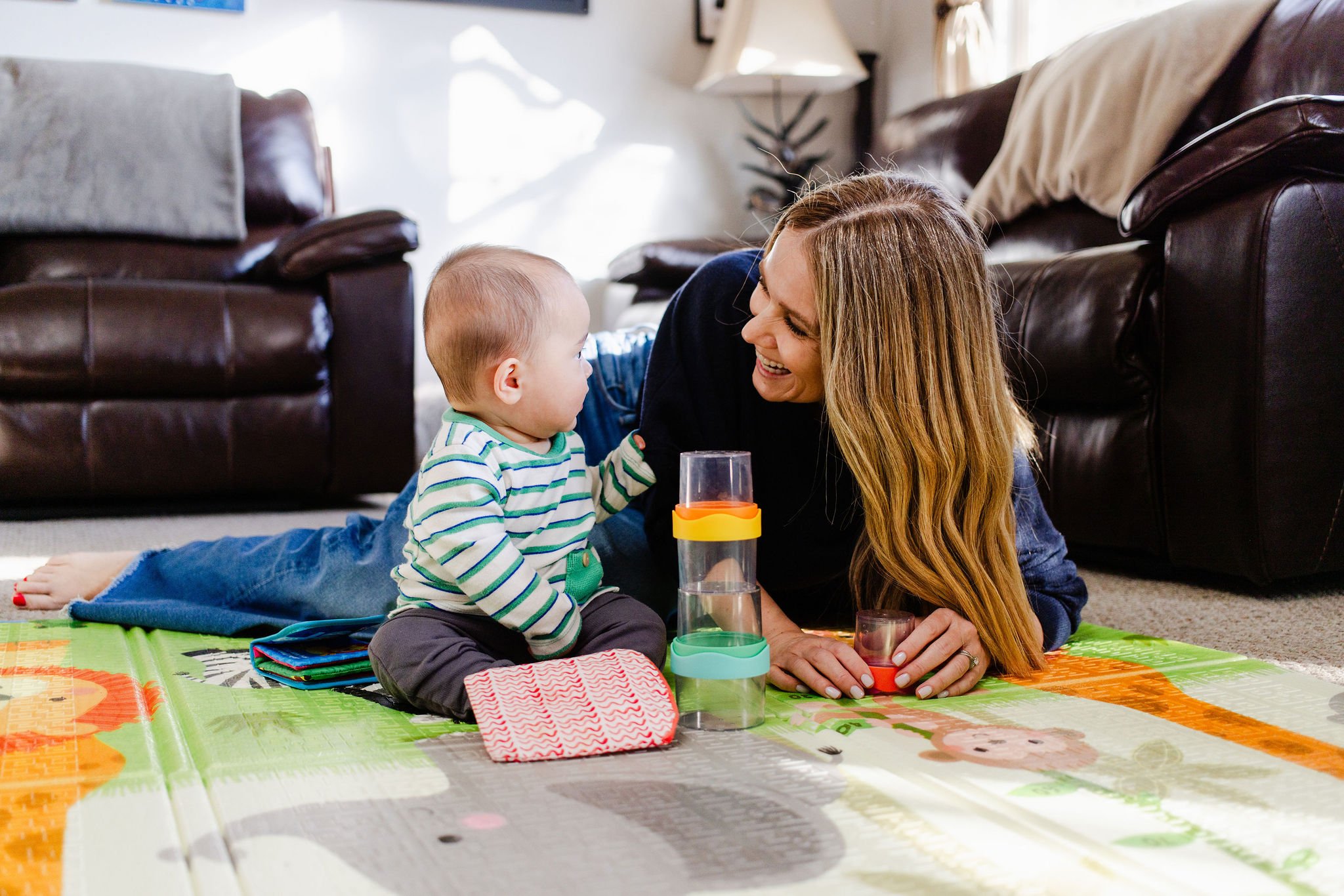 Smiling sleep consultant shares a joyful moment on the play mat with a baby, captured during a cozy brand photography session in Los Angeles.