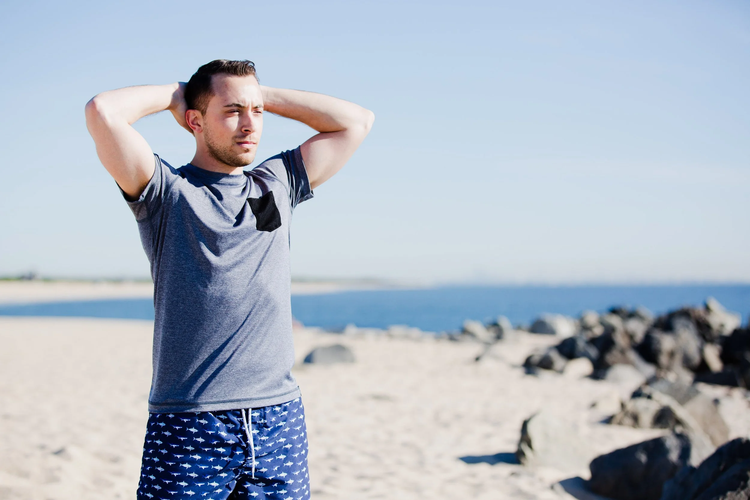 Man stands by the ocean during brand session at Sandy Hook beach boardwalk in NJ, showcasing stylish swimwear