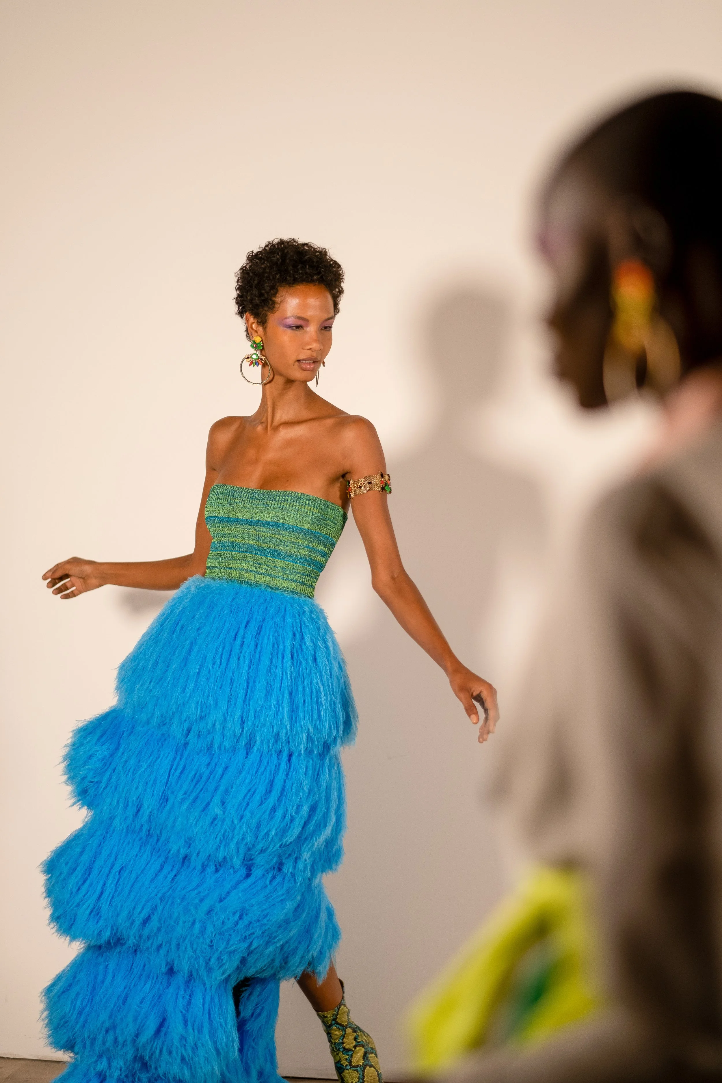 Model wearing a strapless green and blue feathered gown on runway.