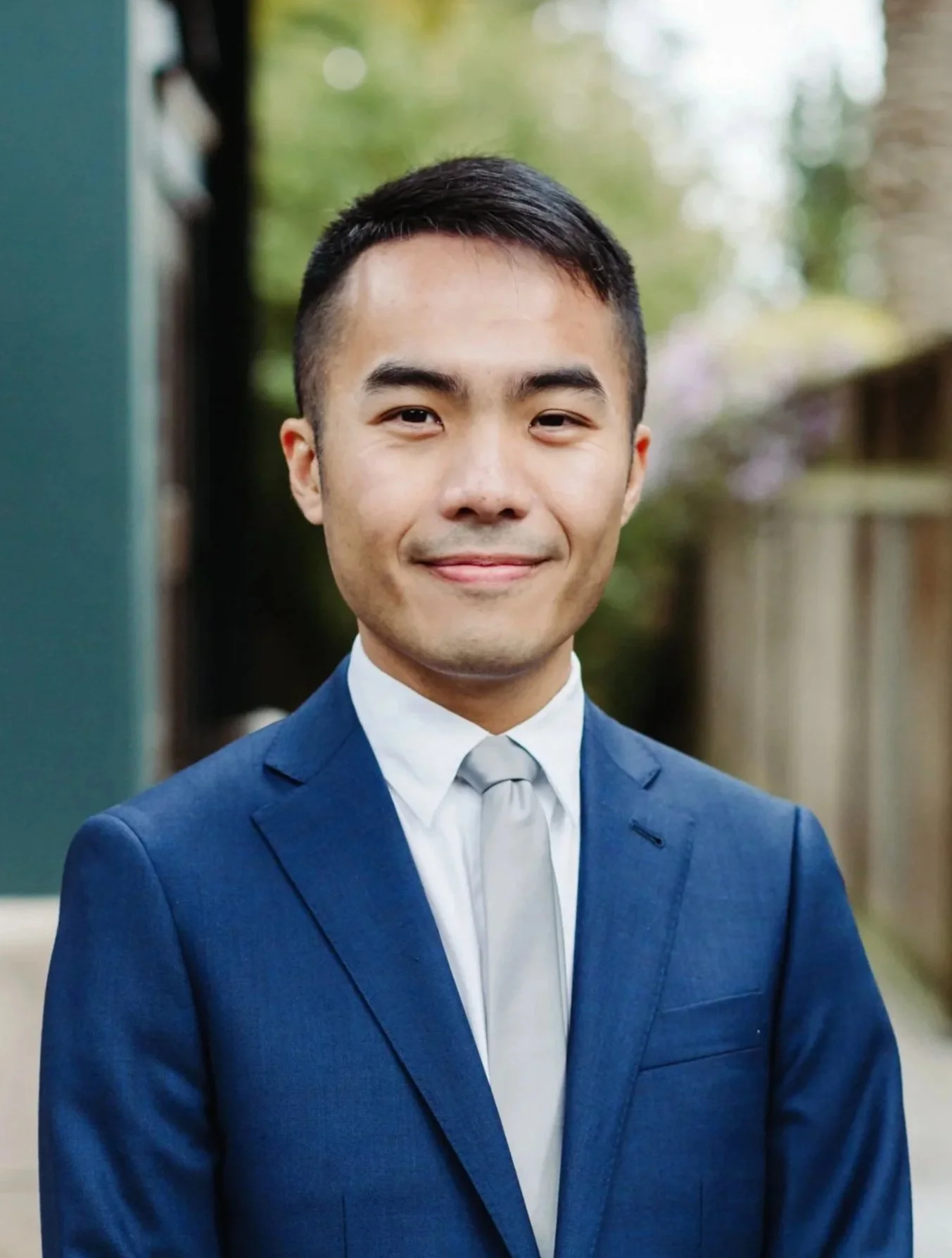 Professional portrait of a smiling man in a dark blue suit, white shirt, and grey tie.