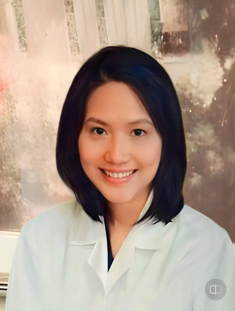 A woman with shoulder-length dark hair and a white lab coat smiling, in front of a painting.