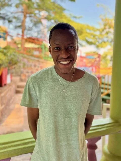 Young person smiling outdoors with colorful playground equipment and trees in the background.