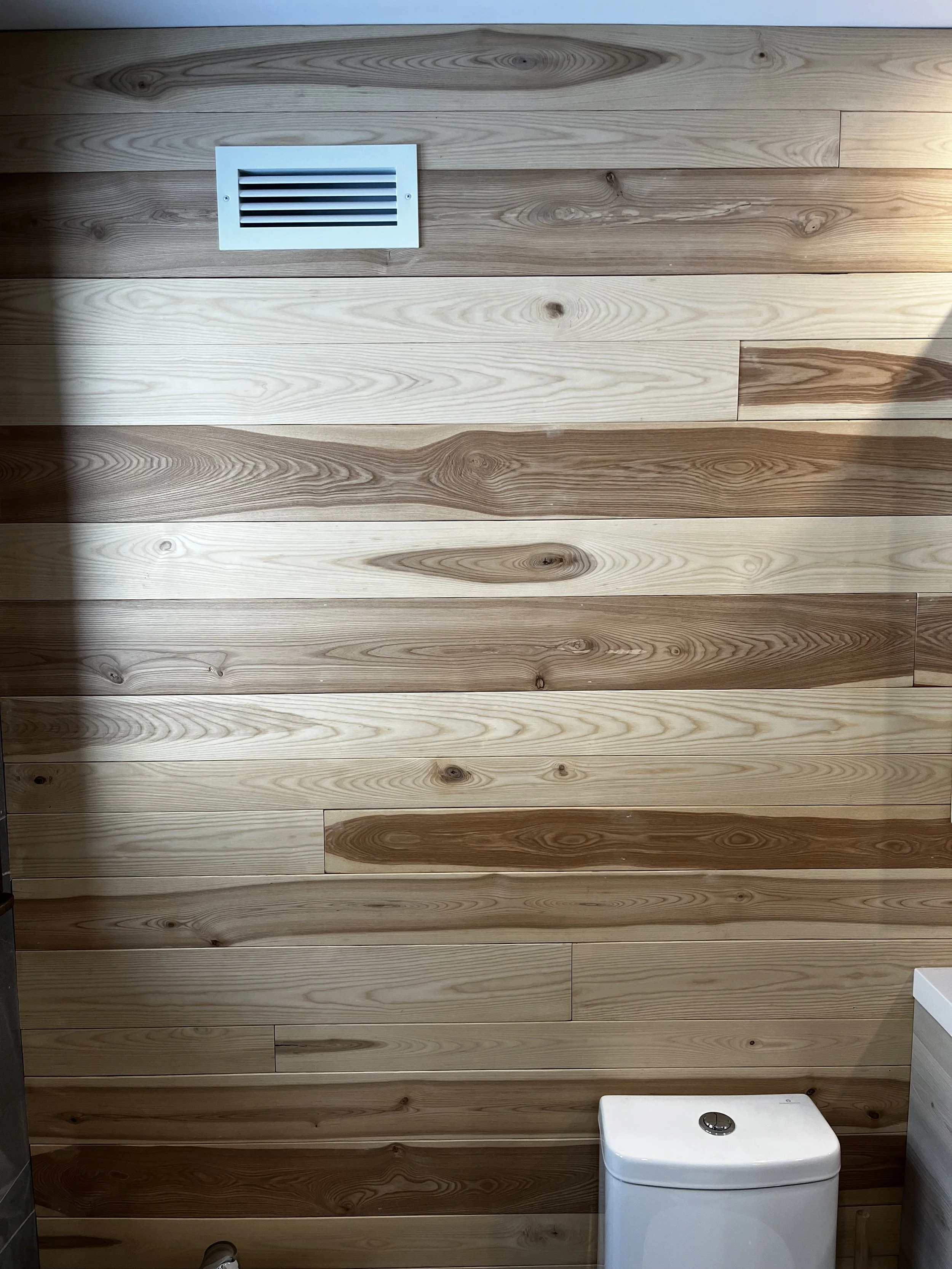 Bathroom with wood panel walls, air vent, and toilet