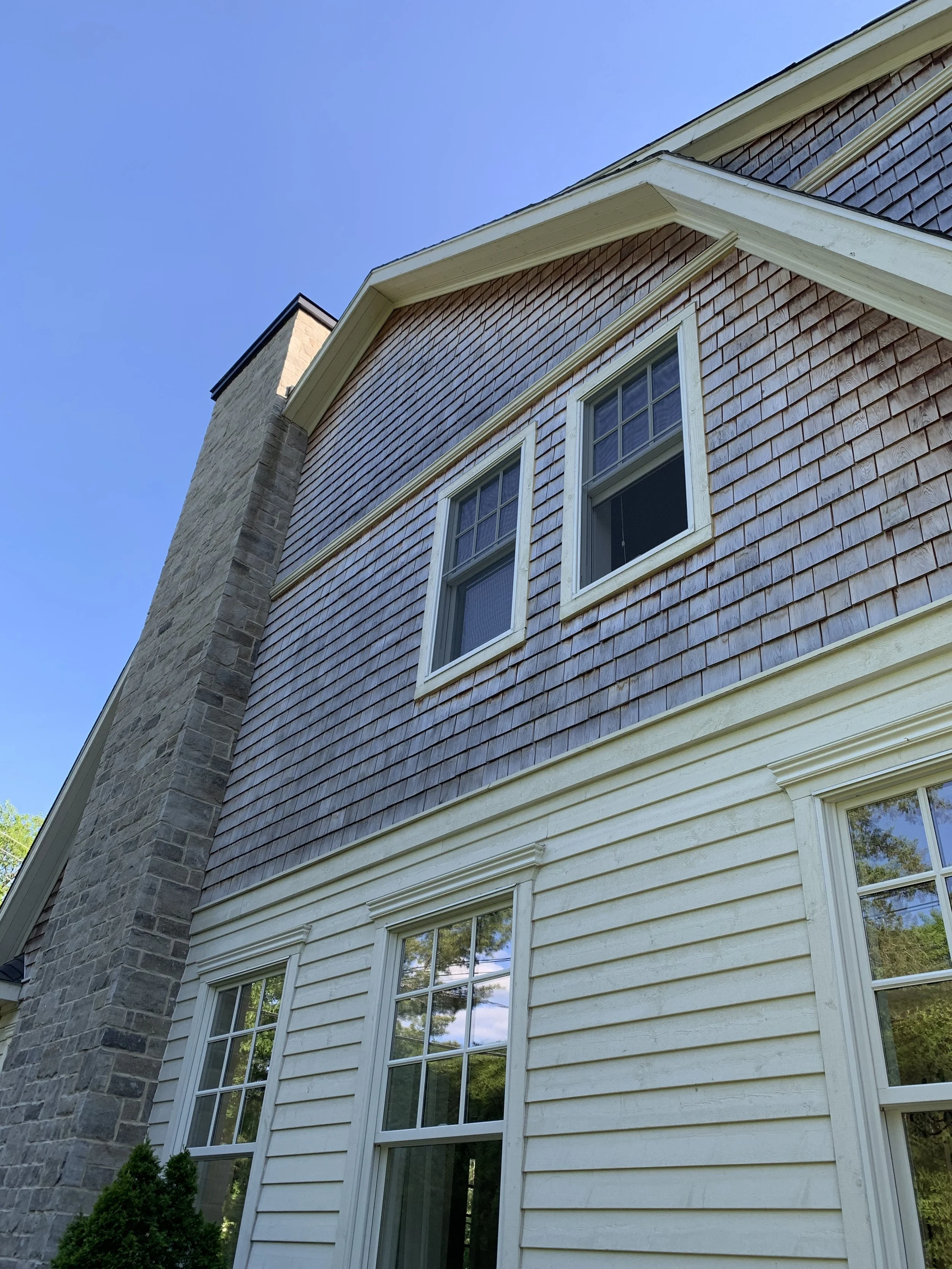 Exterior of a house with wooden siding, stone chimney, and multiple windows.