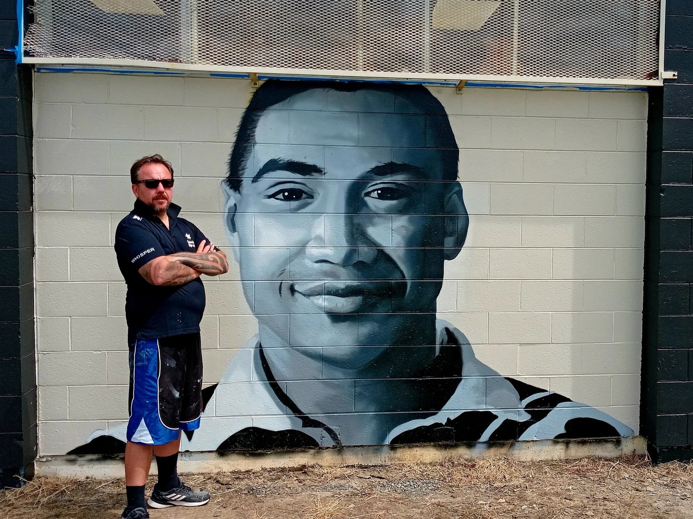 Artist Daniel Dean Allen stands in front of his mural of Esene Faimalo