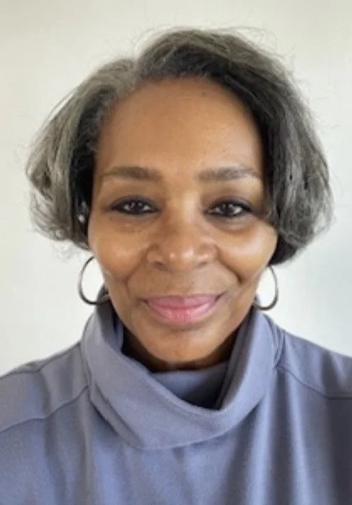 A woman with short, gray hair and hoop earrings smiling at the camera, wearing a gray high-neck top.