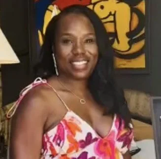 A woman with long black hair smiling and wearing a colorful pink and orange floral dress.