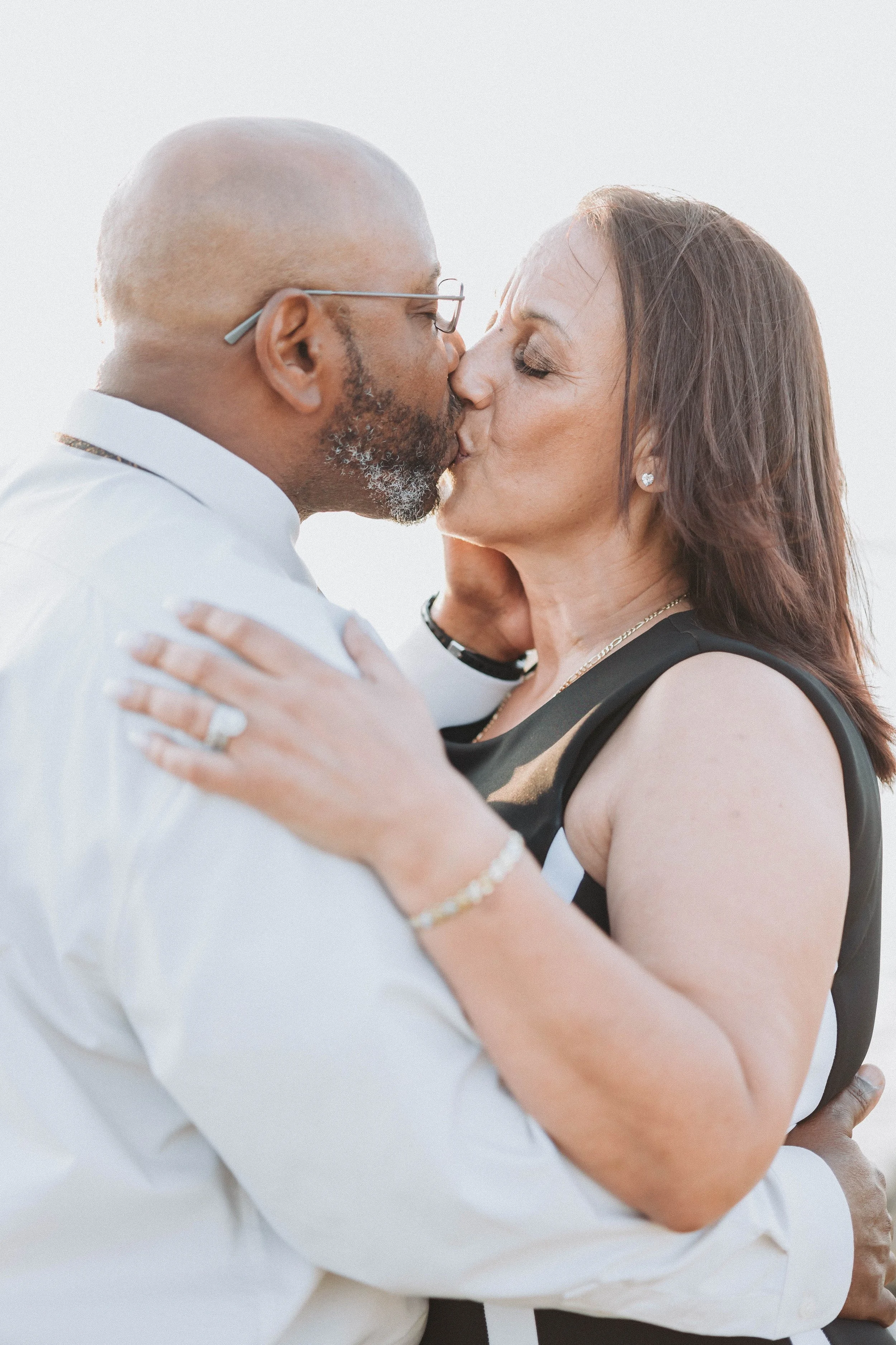 A couple kissing outdoors, wearing formal attire.