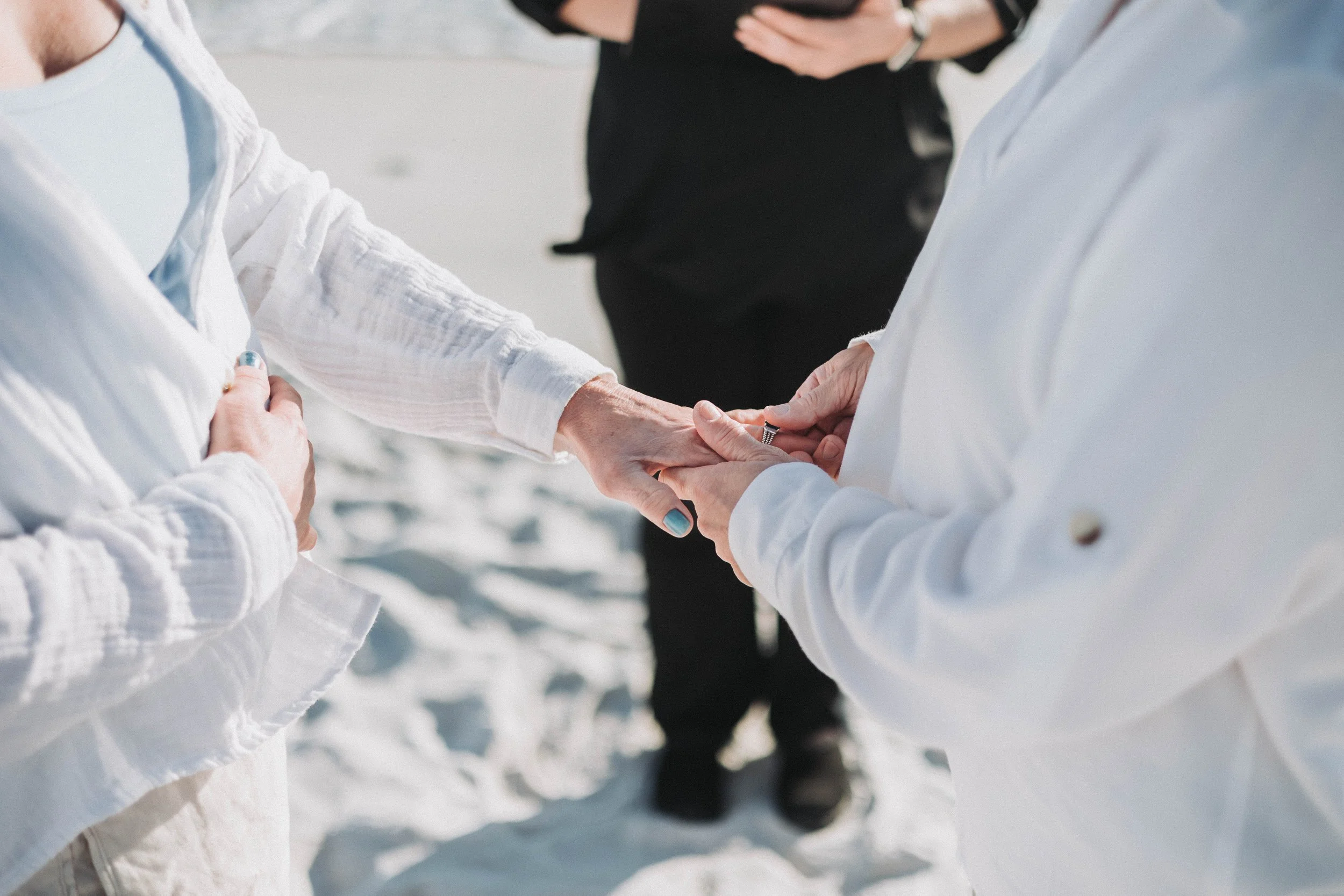 Close-up of two people in white exchanging rings during a beach wedding ceremony.