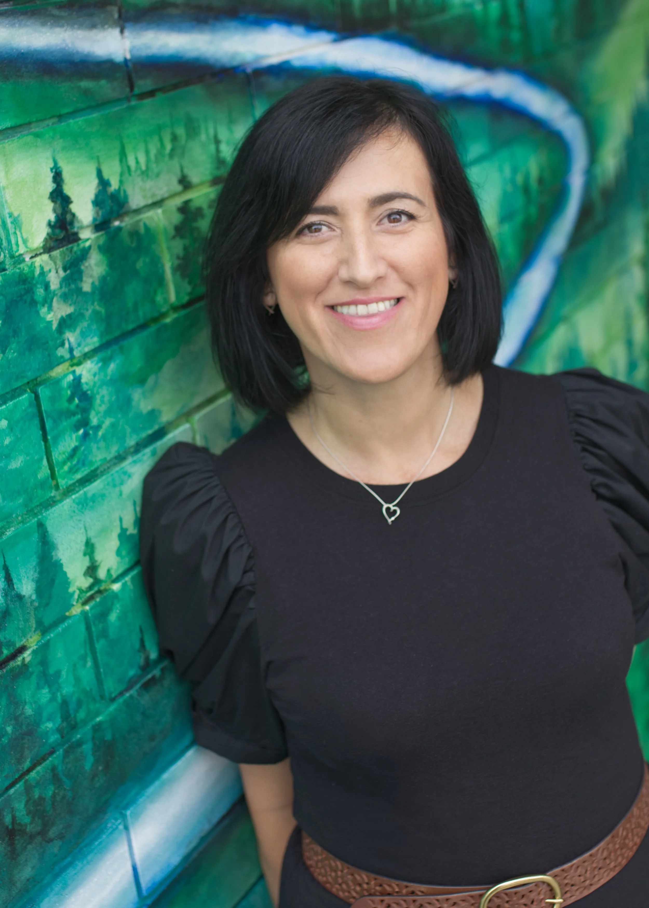 woman with short, black hair in a black shirt smiling in front of a green wall
