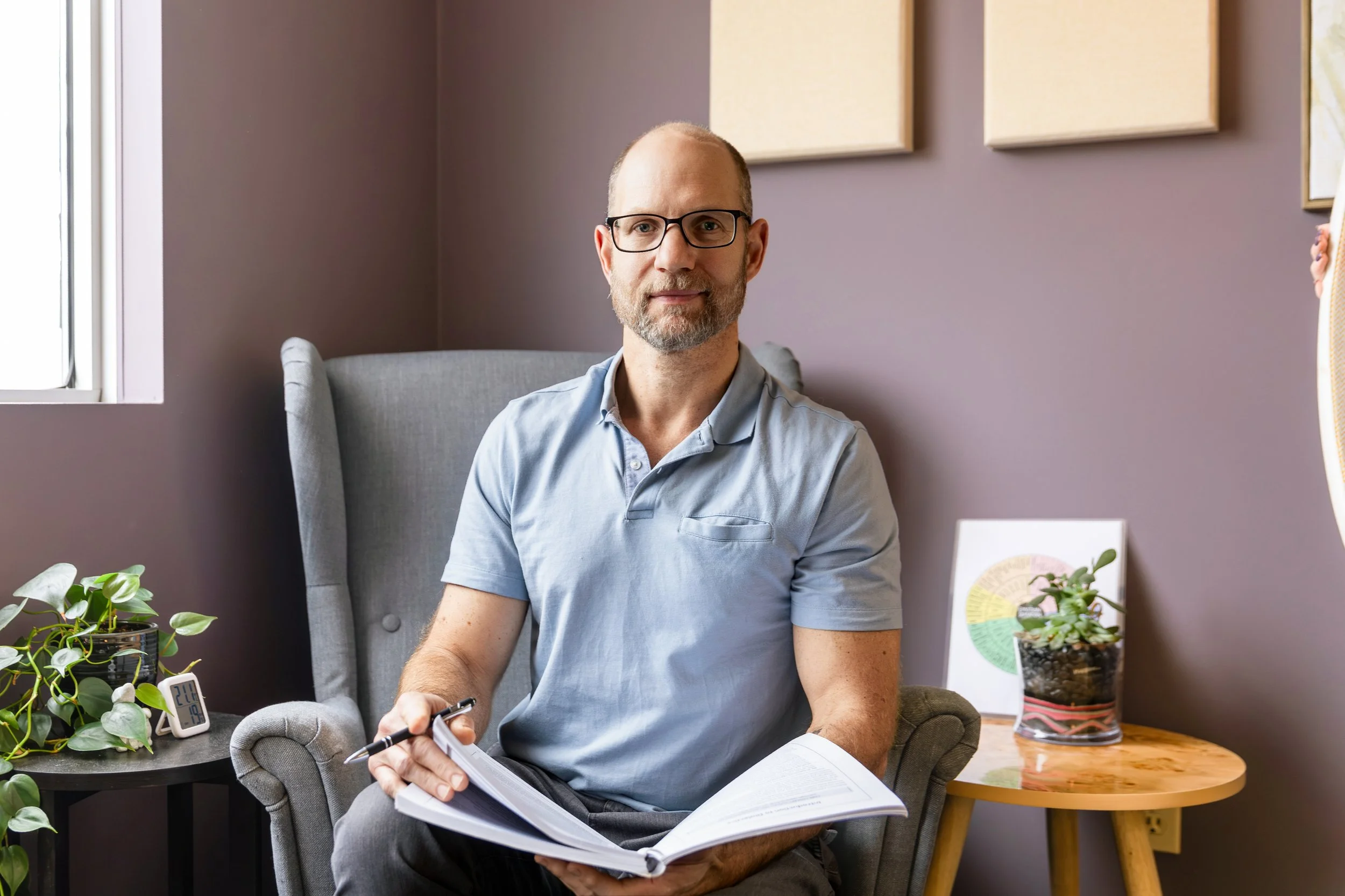 Close-up photo of a man wearing a blue cap, sunglasses on top, and a blue plaid shirt, outdoors with trees and a clear blue sky.