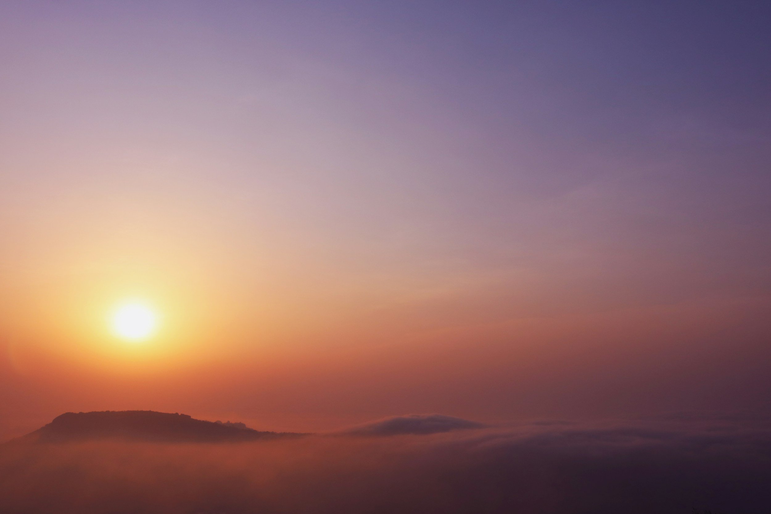 Sun setting behind a mountain with a colorful sky and clouds.