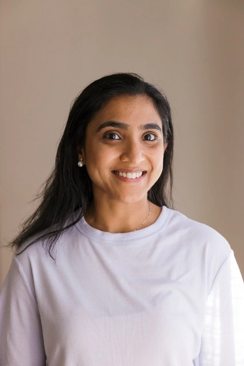Young woman with long dark hair, smiling, sitting on grass, holding a black dog. Yoga in the Blue Mountains.