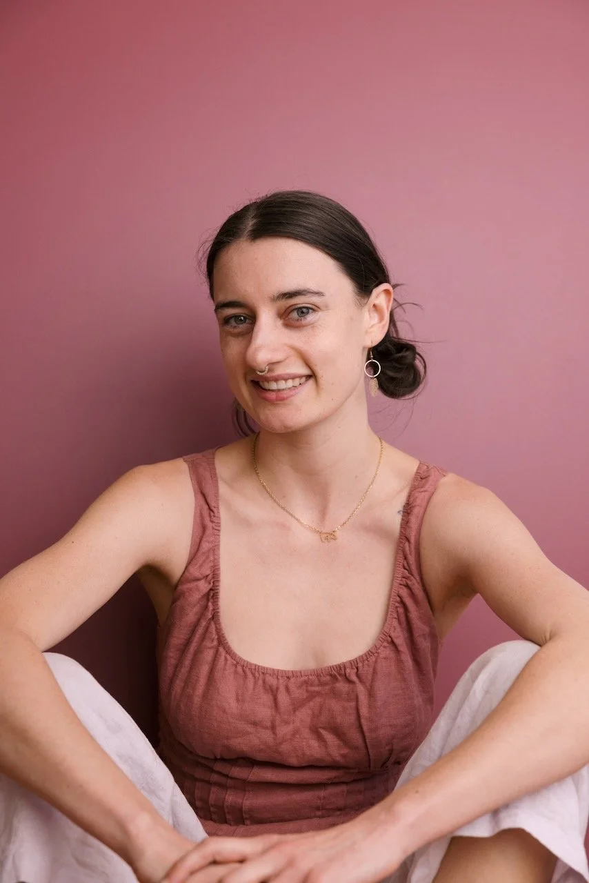 A woman with dark hair lying on a bed of rocks and smiling at the camera. Yoga in the Blue Mountains.