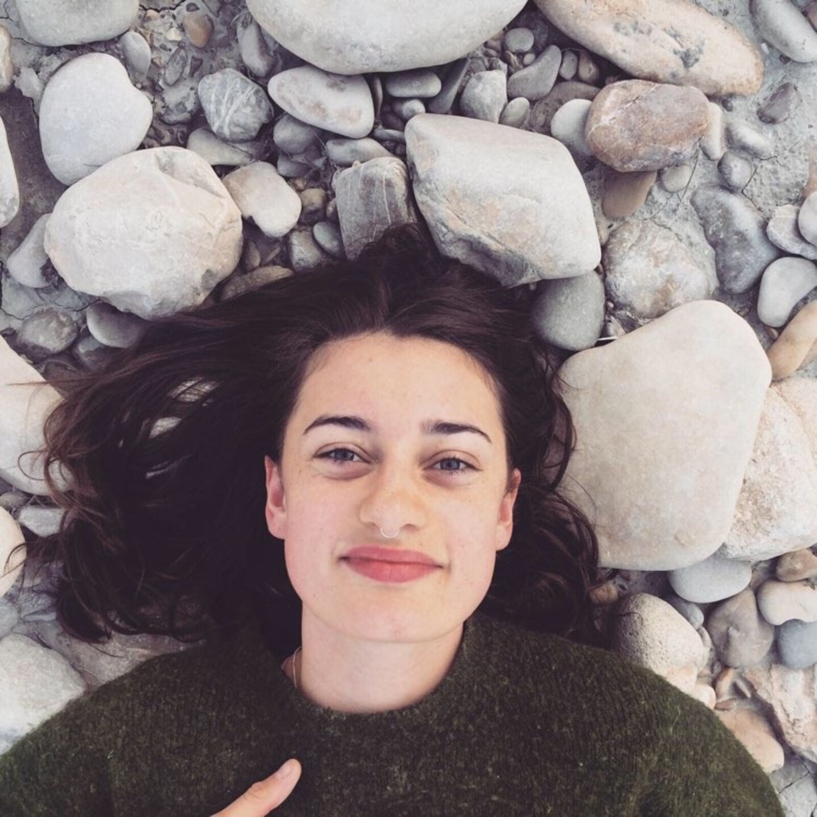 A woman with dark hair lying on a bed of rocks and smiling at the camera. Yoga in the Blue Mountains.