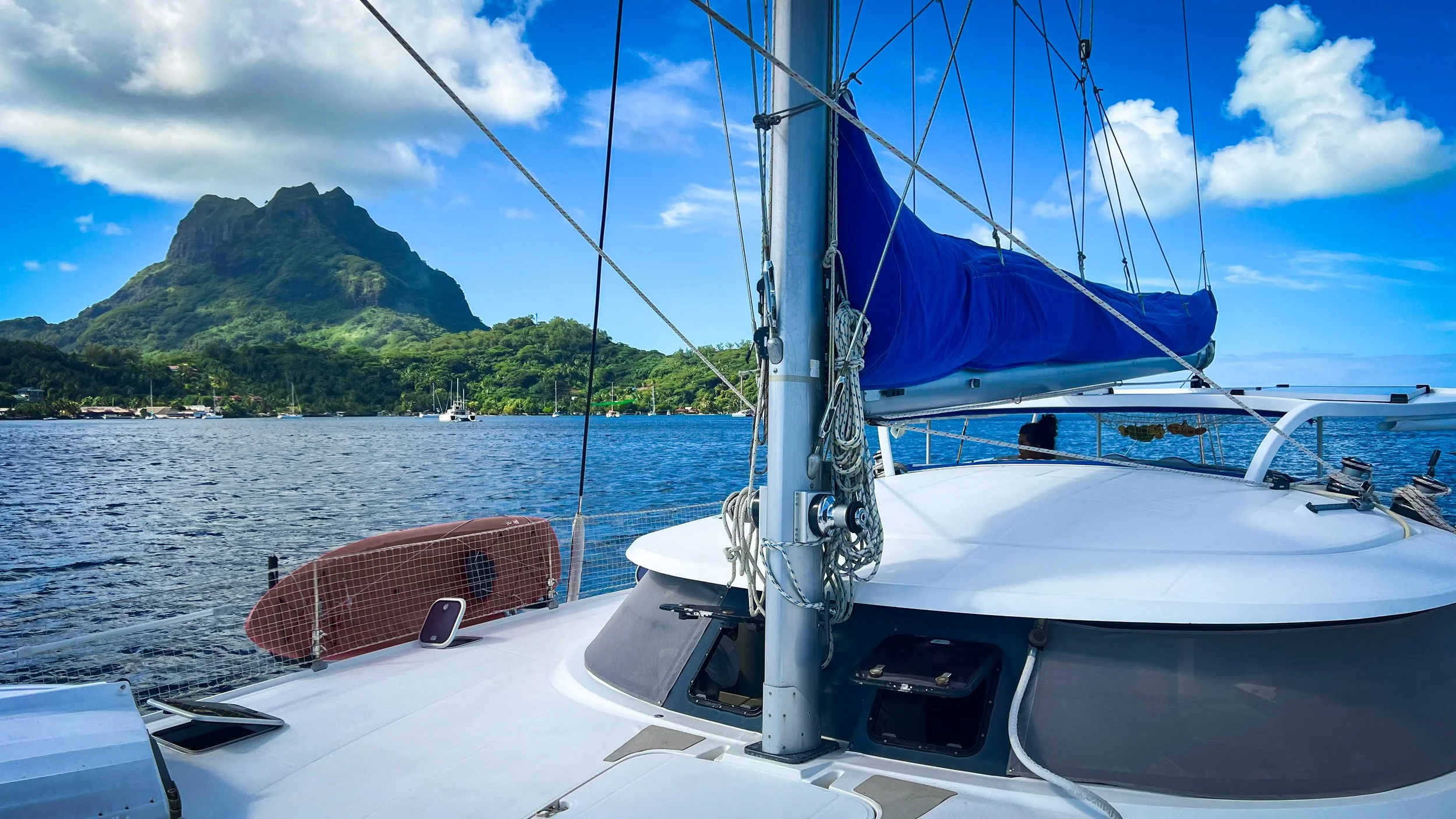 taken from deck of white catamaran sailboat sailing in bora bora lagoon with green tropical mountain beyond