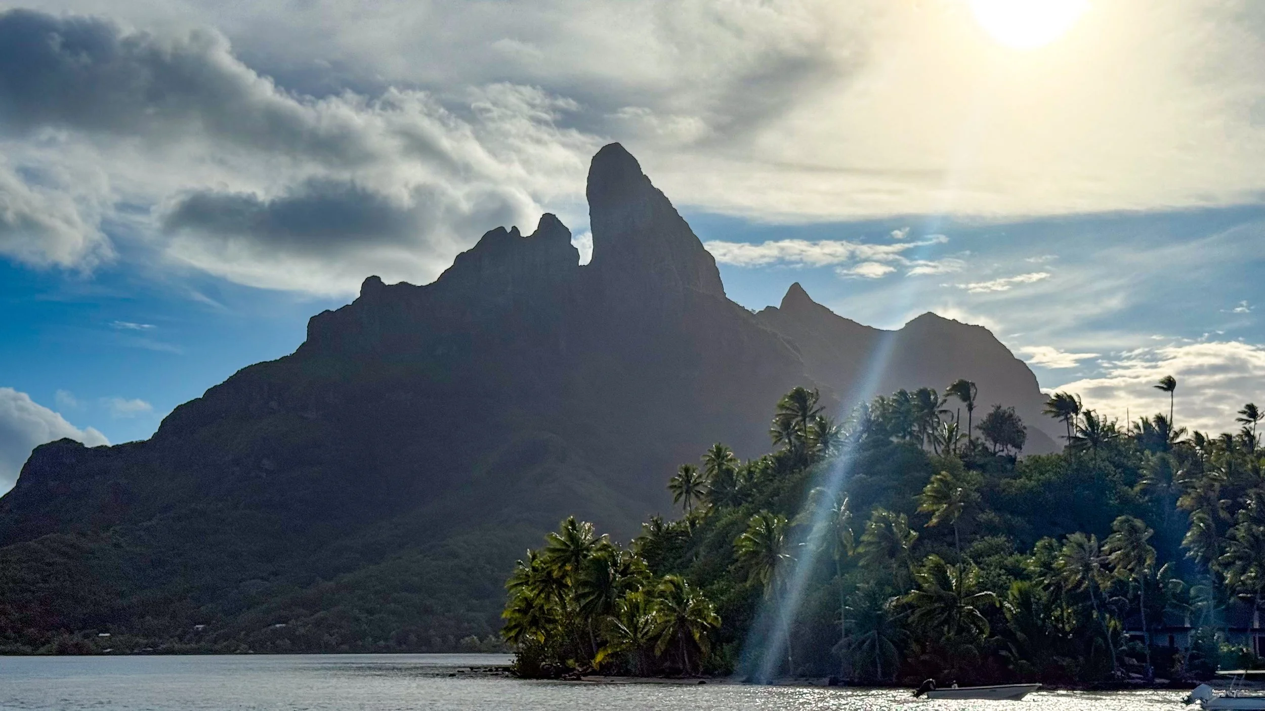 Bora Bora mountain with palm tree island in front and dramatic sun rays.