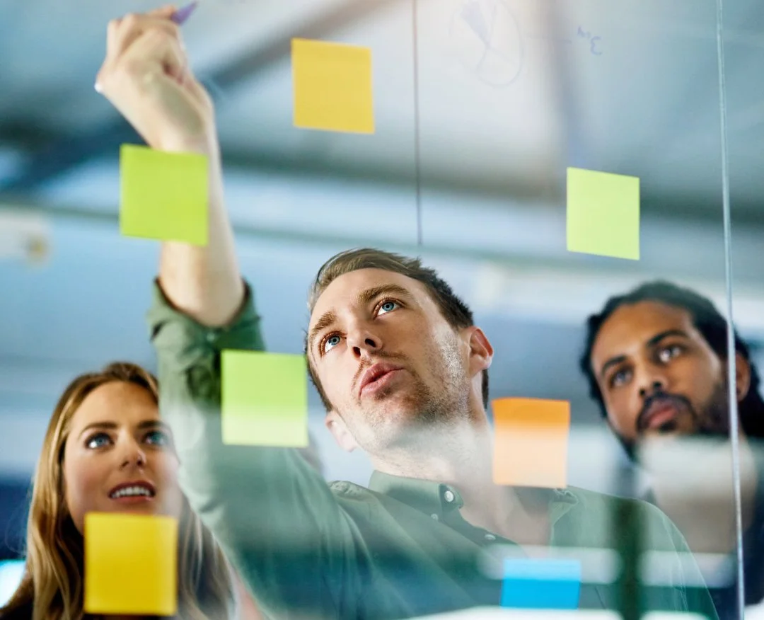 People collaborating and writing on sticky notes on a glass wall in a modern office.