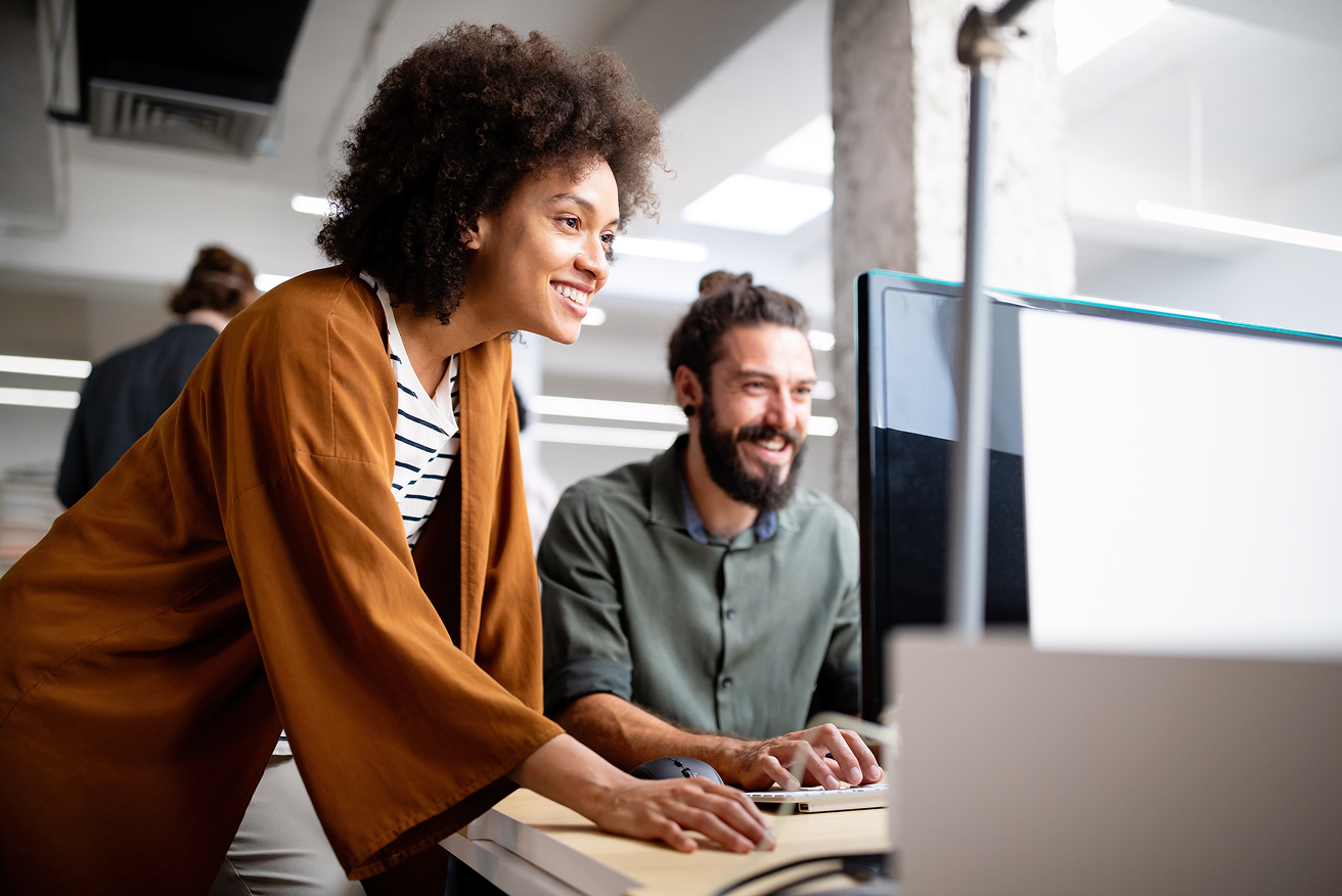 Two colleagues looking at a computer monitor and smiling in an office.