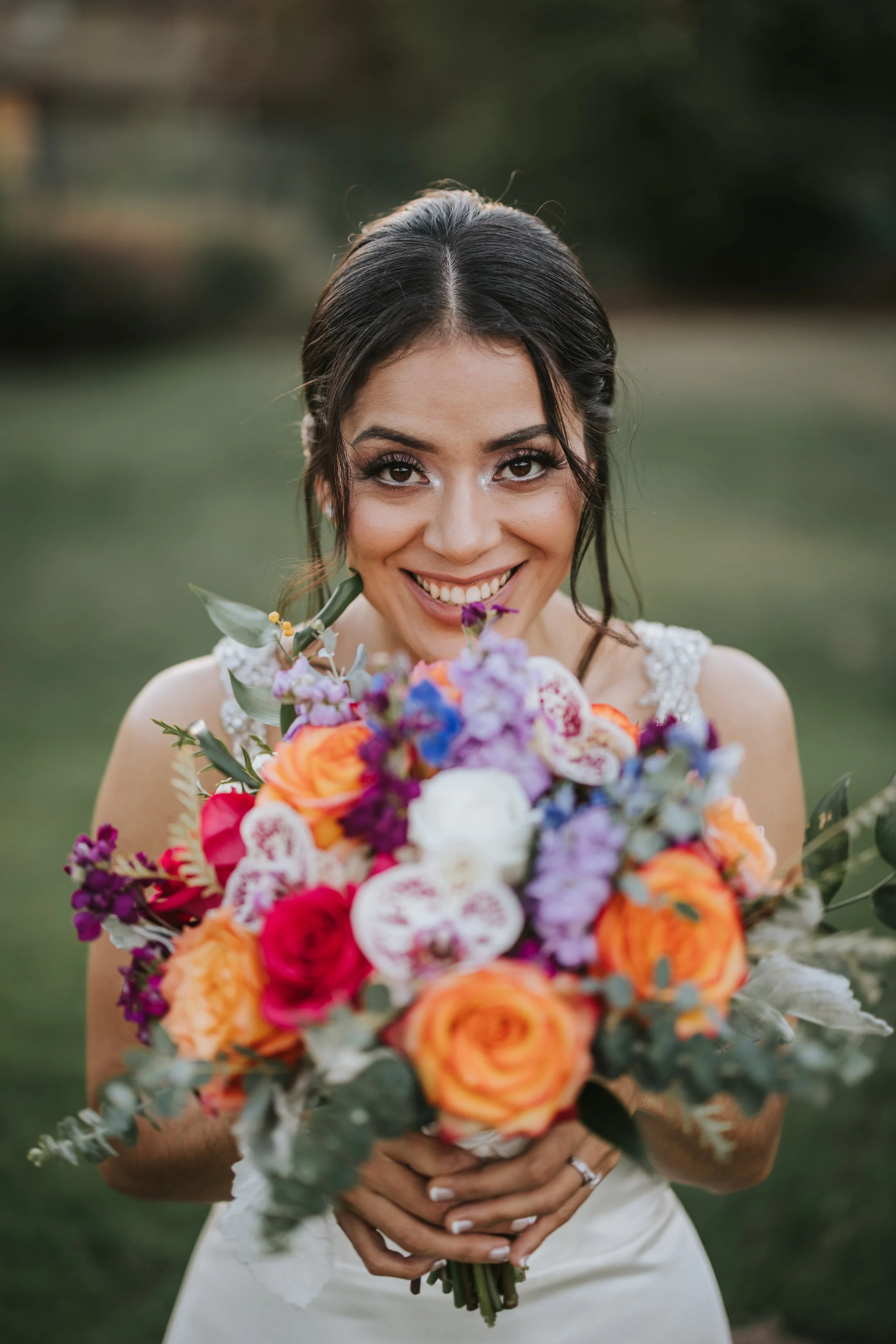 A happy bride holding a colorful bouquet of flowers outdoors.