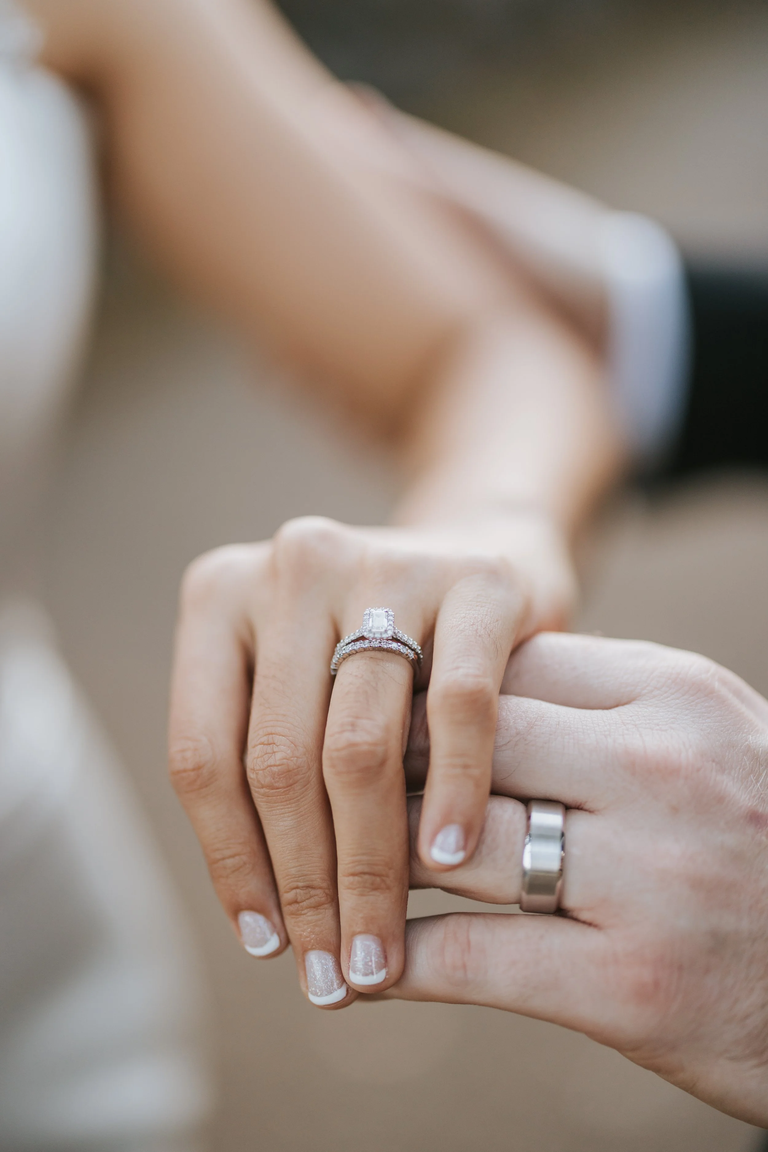 Close-up of a woman's hand with an engagement ring and wedding band, holding a man's hand with a wedding band.