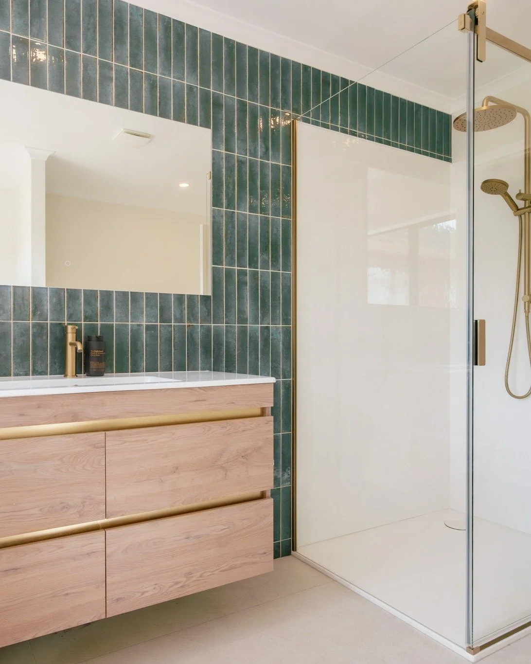 A stunning Waimauku bathroom renovation with rich teal feature wall tiles, soft cream textured half-height tiles, and luxe brushed brass fittings throughout &ndash; from mixers to shower doors and heated towel rails. Loving this perfect blend of bold
