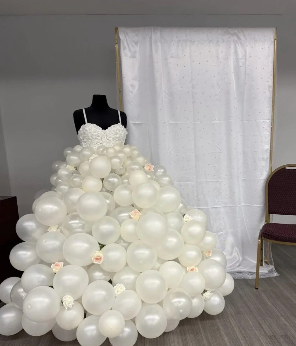 A dress made of white balloons with pink and white roses, displayed on a mannequin against a white backdrop.