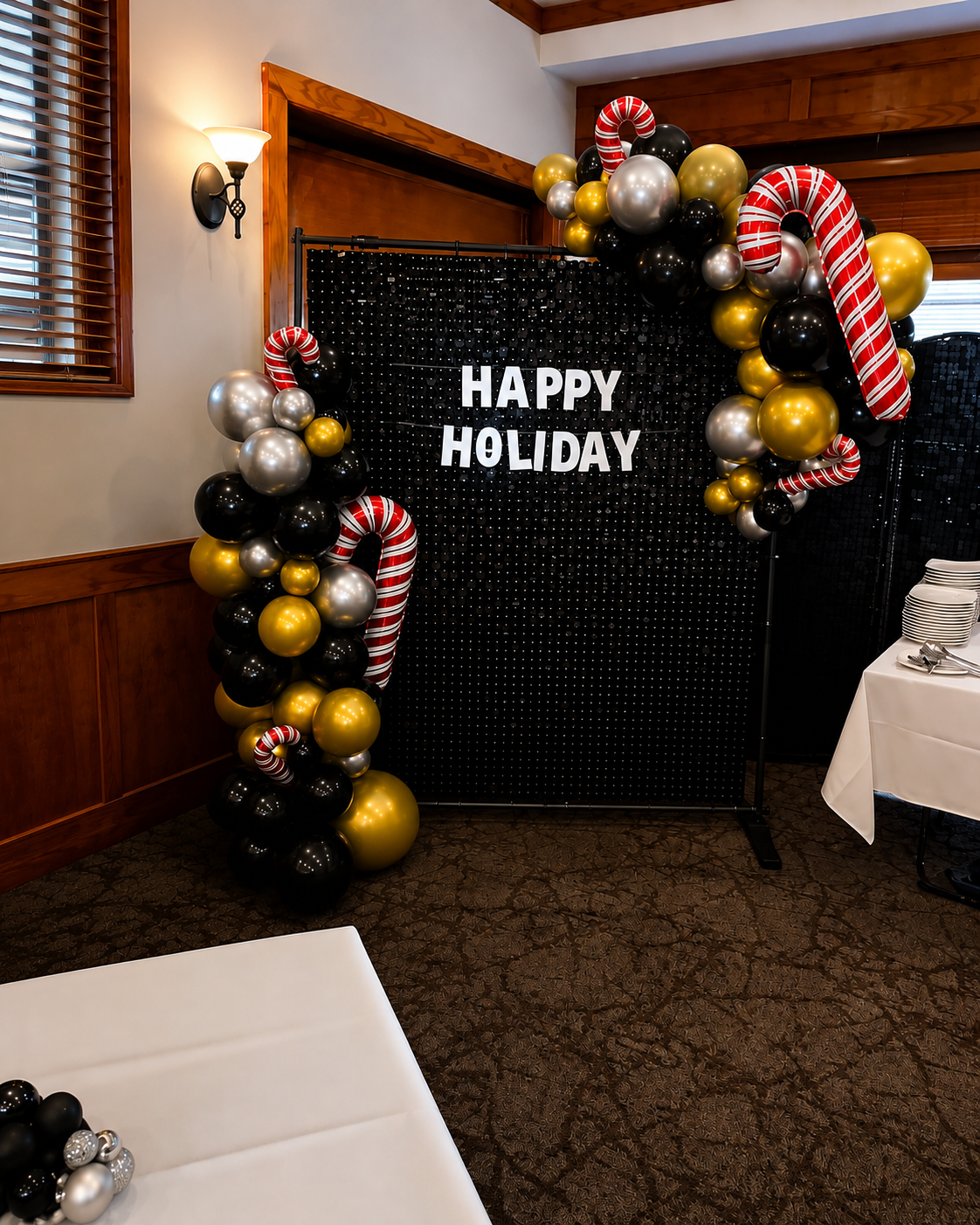Holiday greeting display with black backdrop, white letters saying 'HAPPY HOLIDAY', decorated with black, gold, silver, and red and white striped balloons and candy cane-themed balloons.