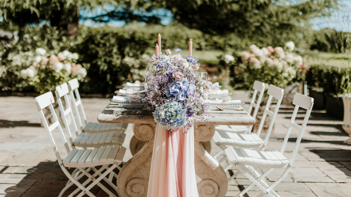 Outdoor dining table decorated with pastel-colored flowers and candles for a celebration.