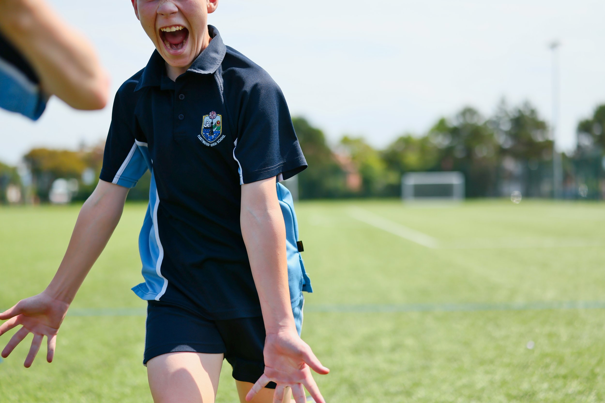 Young boy in a navy blue sports uniform laughing on a grassy field.