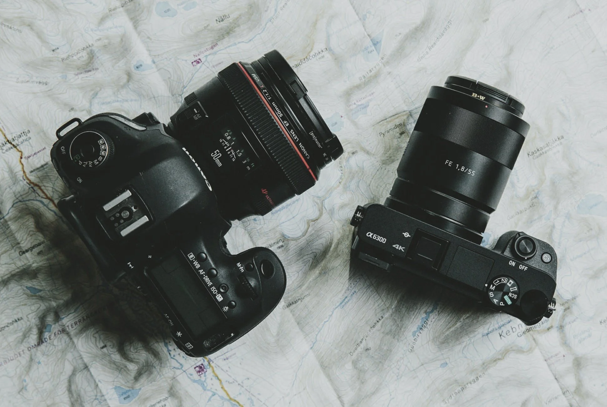 Two cameras with lenses placed on a map background, including a Canon DSLR and a Sony mirrorless camera.