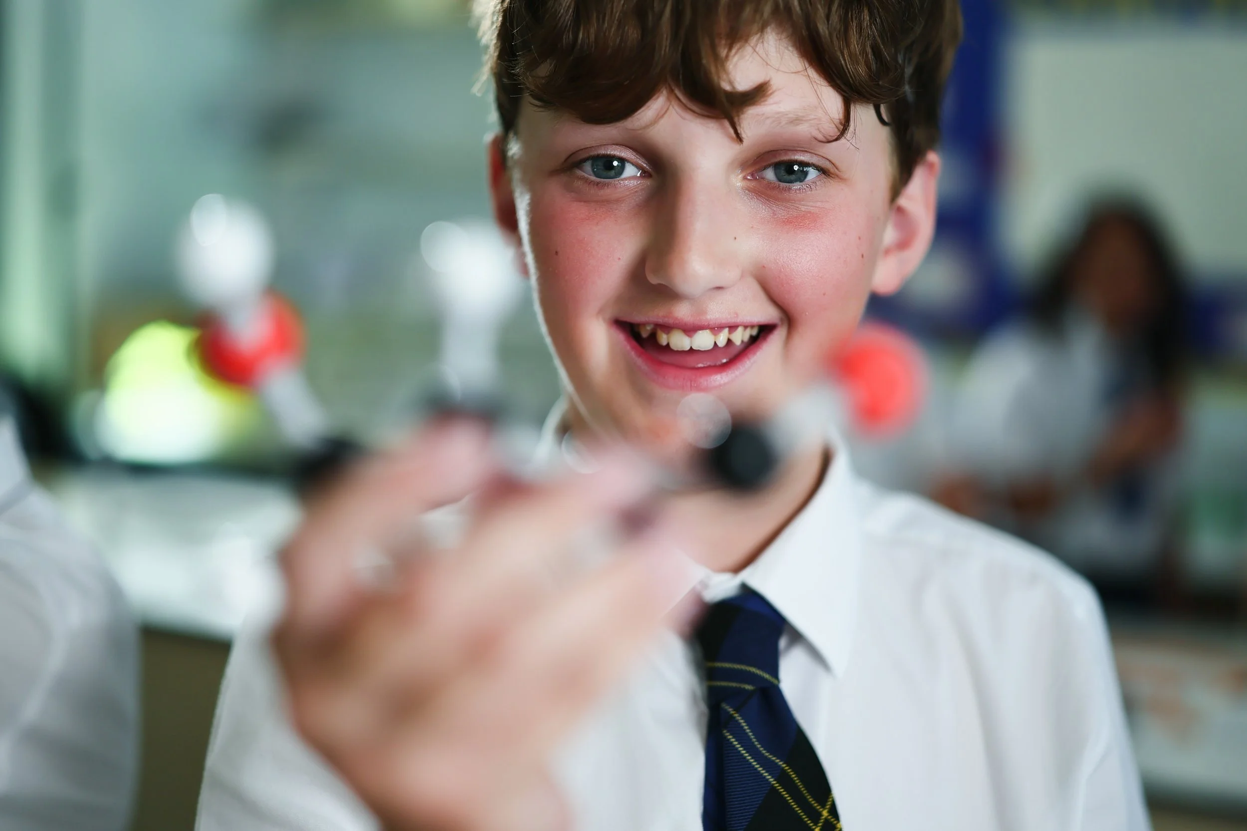 A young boy with brown hair and blue eyes smiling as he holds a small robot in front of him.
