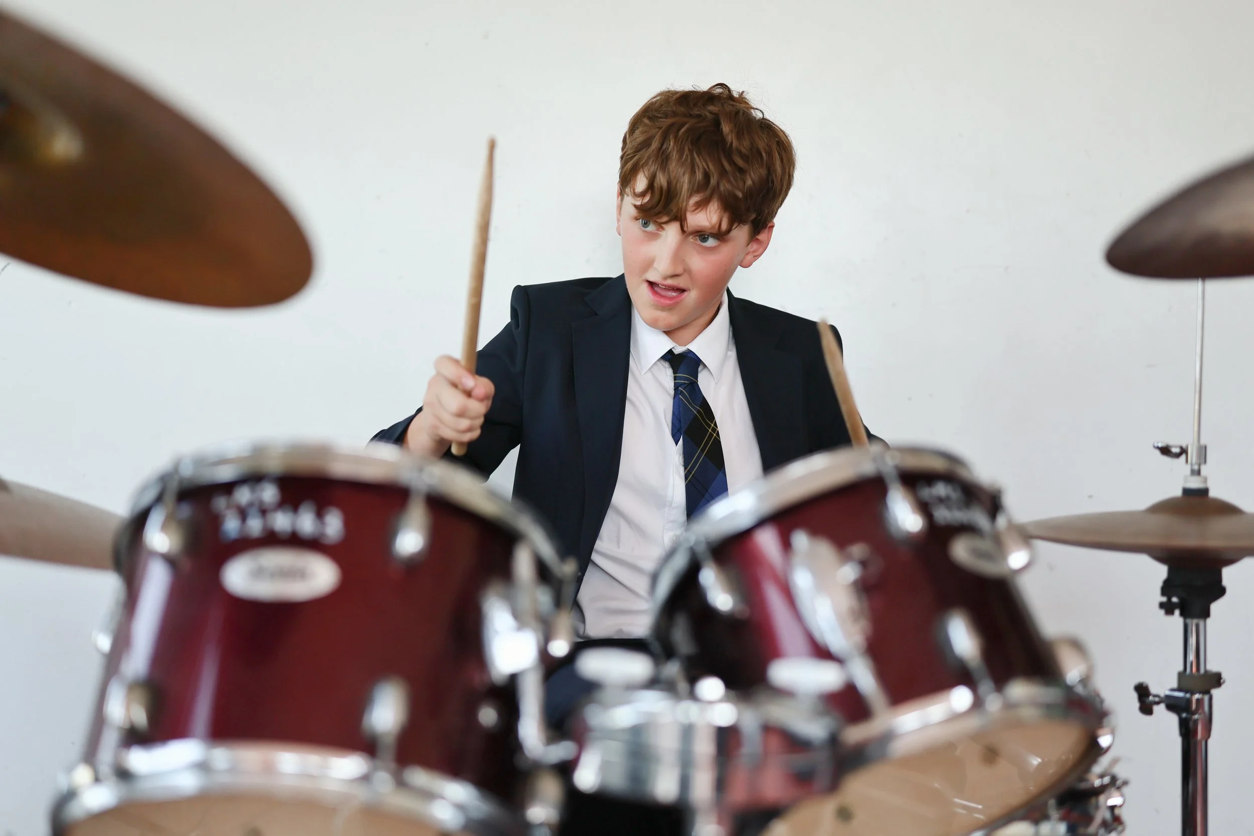 Young boy in a suit playing a drum set.