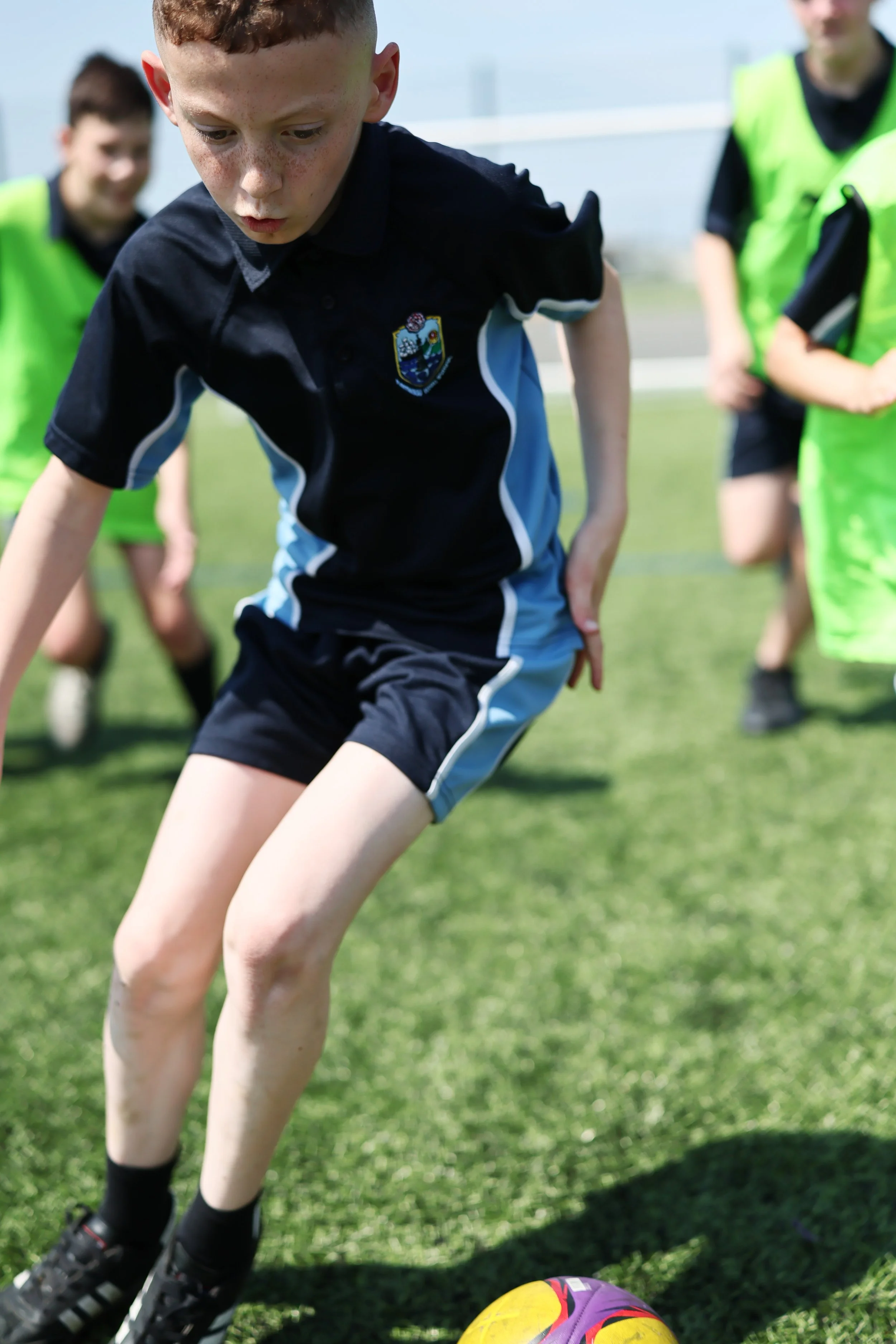 Young boys playing soccer outdoors on a grass field, with one boy in the foreground about to kick a colorful soccer ball.