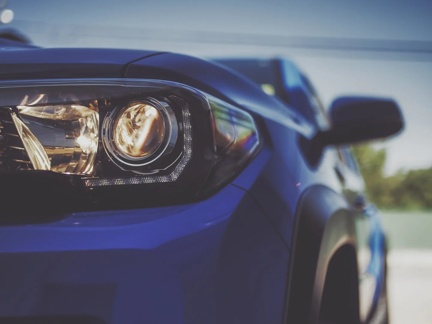 Close-up of a blue car's front headlight with a blurred background.