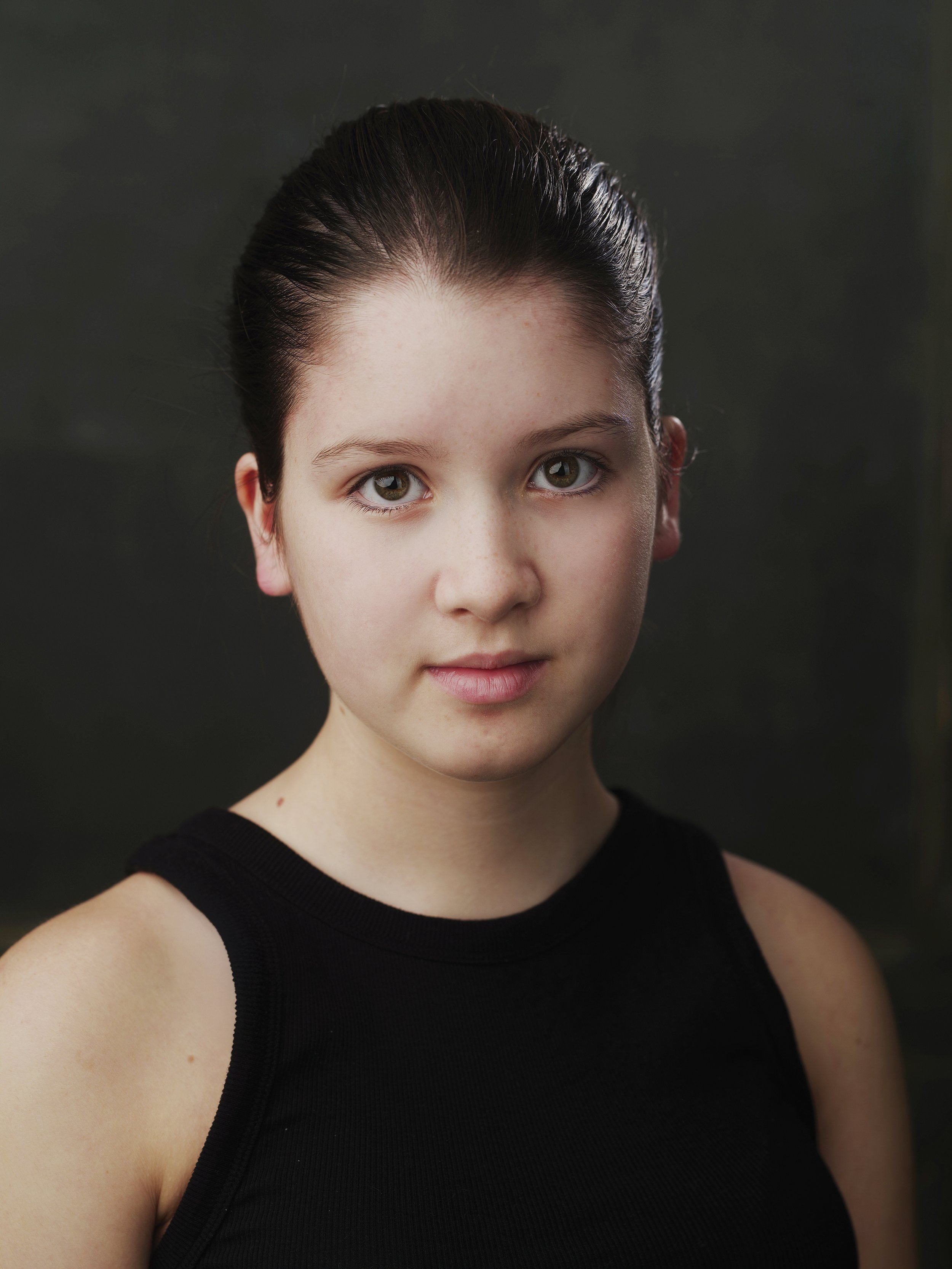 Portrait of a young person with dark hair, wearing a black tank top, against a dark background.