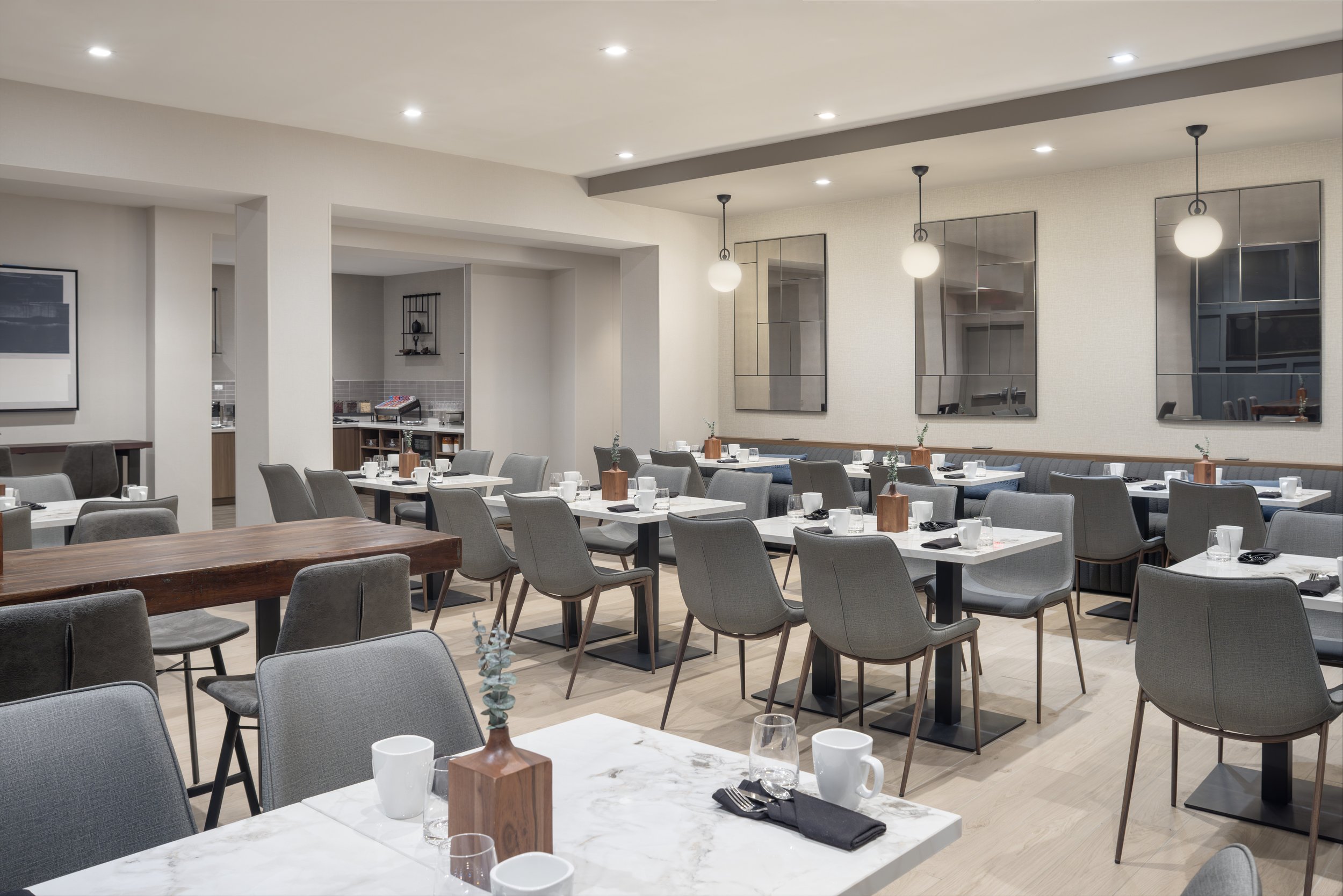 Dine-in restaurant with tables set for service, decorated with glasses, plates, and cutlery, featuring modern lighting fixtures and artwork on the walls.