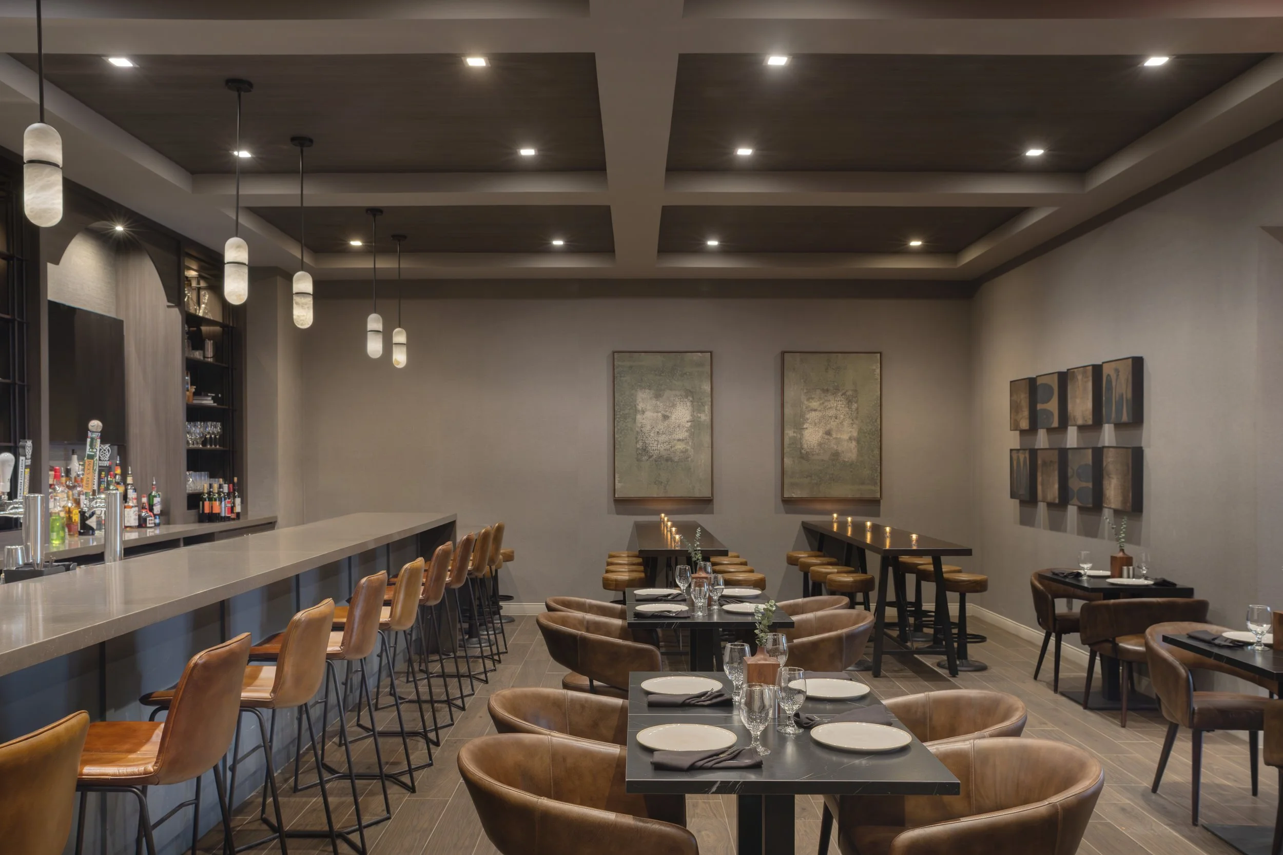 Empty bar with chairs and tables, decorated with modern lighting and artwork, with a patterned carpet and a bar counter in the background, overlaid with text 'PHOTO COMING SOON'.
