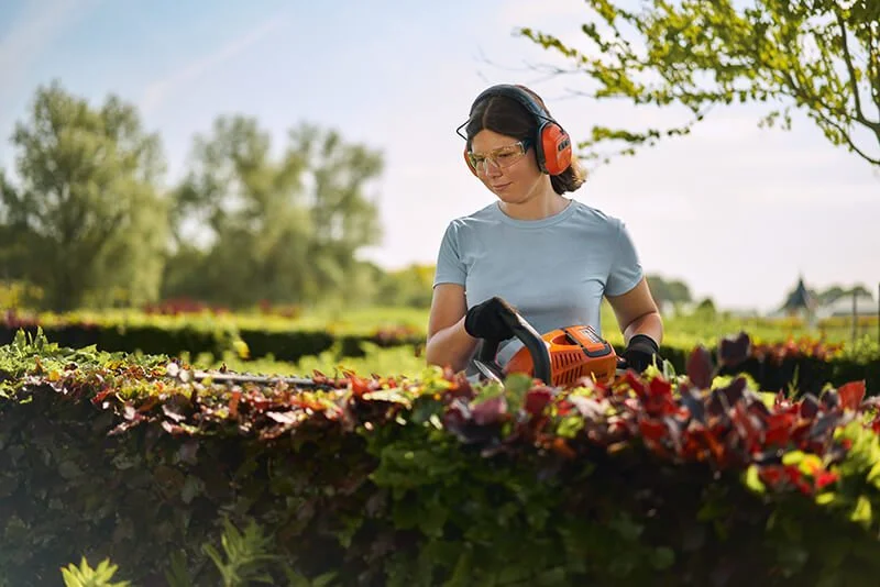 Vrouw met gehoorbeschermer en veiligheidsbril snoeit planten in een tuin of veld