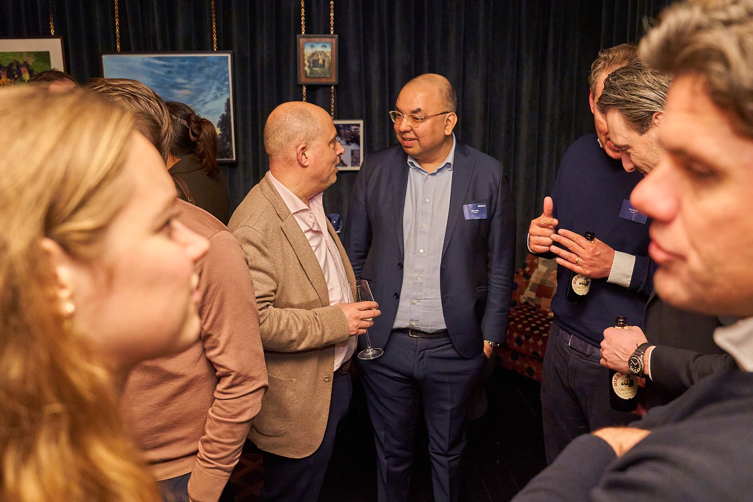 Een groep mensen die in een kring aan het praten zijn tijdens een netwerkevenement, in een kamer met kunstwerken aan de muur.