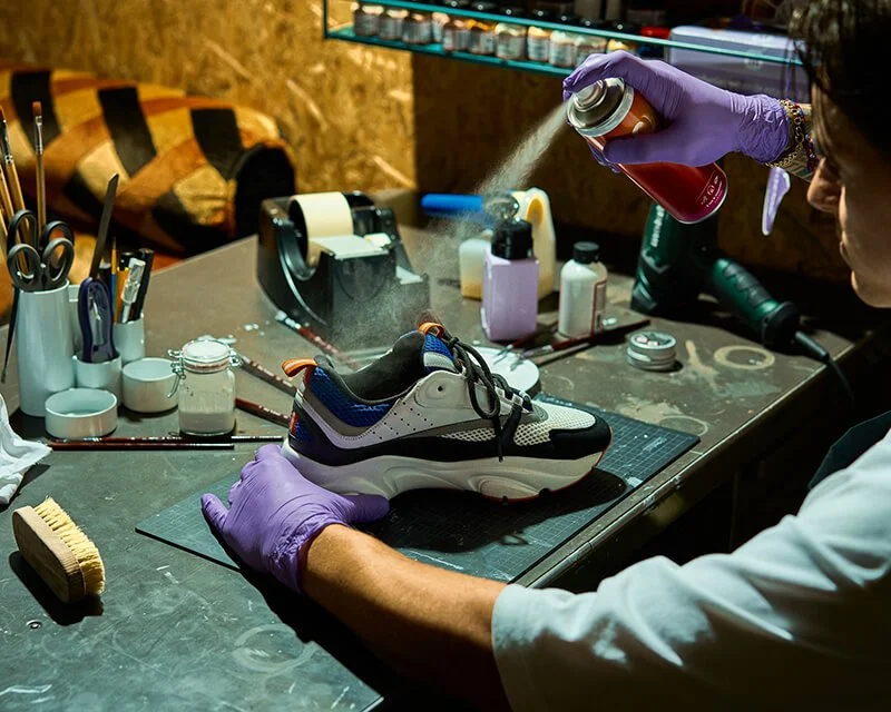 Een persoon die schoenen schoonmaakt of verzorgt in een werkplaats met verschillende gereedschappen en materialen.